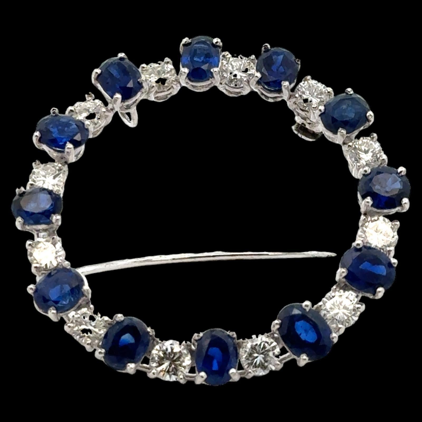 1960's diamond and sapphire brooch handcrafted in platinum. The pin features 12 round brilliant cut diamonds weighing approximately 3.00 carat total weight and graded G-H color and VS2-SI1 clarity. The diamonds alternate with 12 oval sapphires