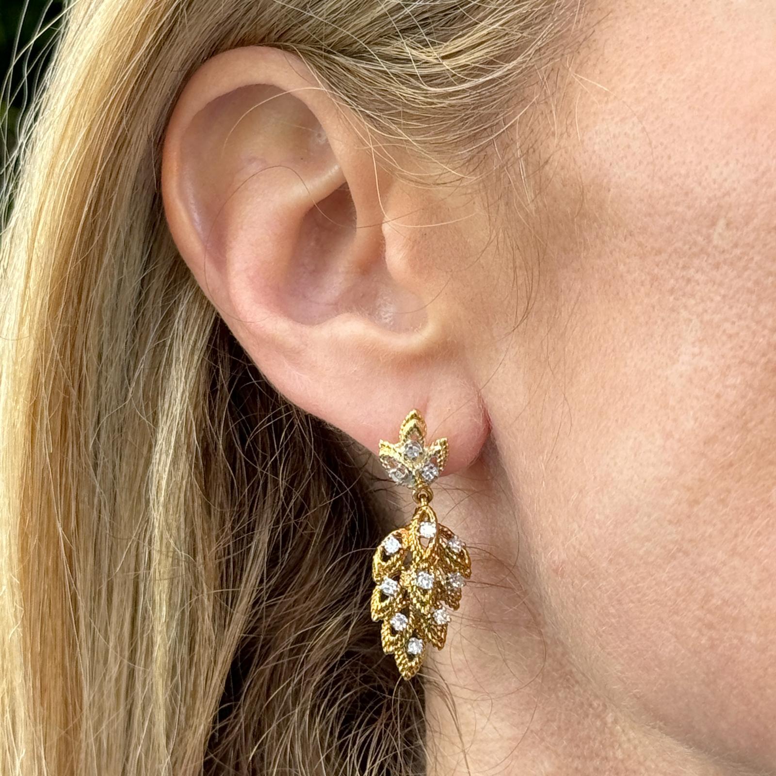 Diamond leaf motif dangle earrings are handcrafted in 14 karat yellow gold. The earrings feature 24 single cut round diamonds weighing approximatley .70 carat total weight and graded H-I color and SI clarity. The earrings measure 1.50 inches in