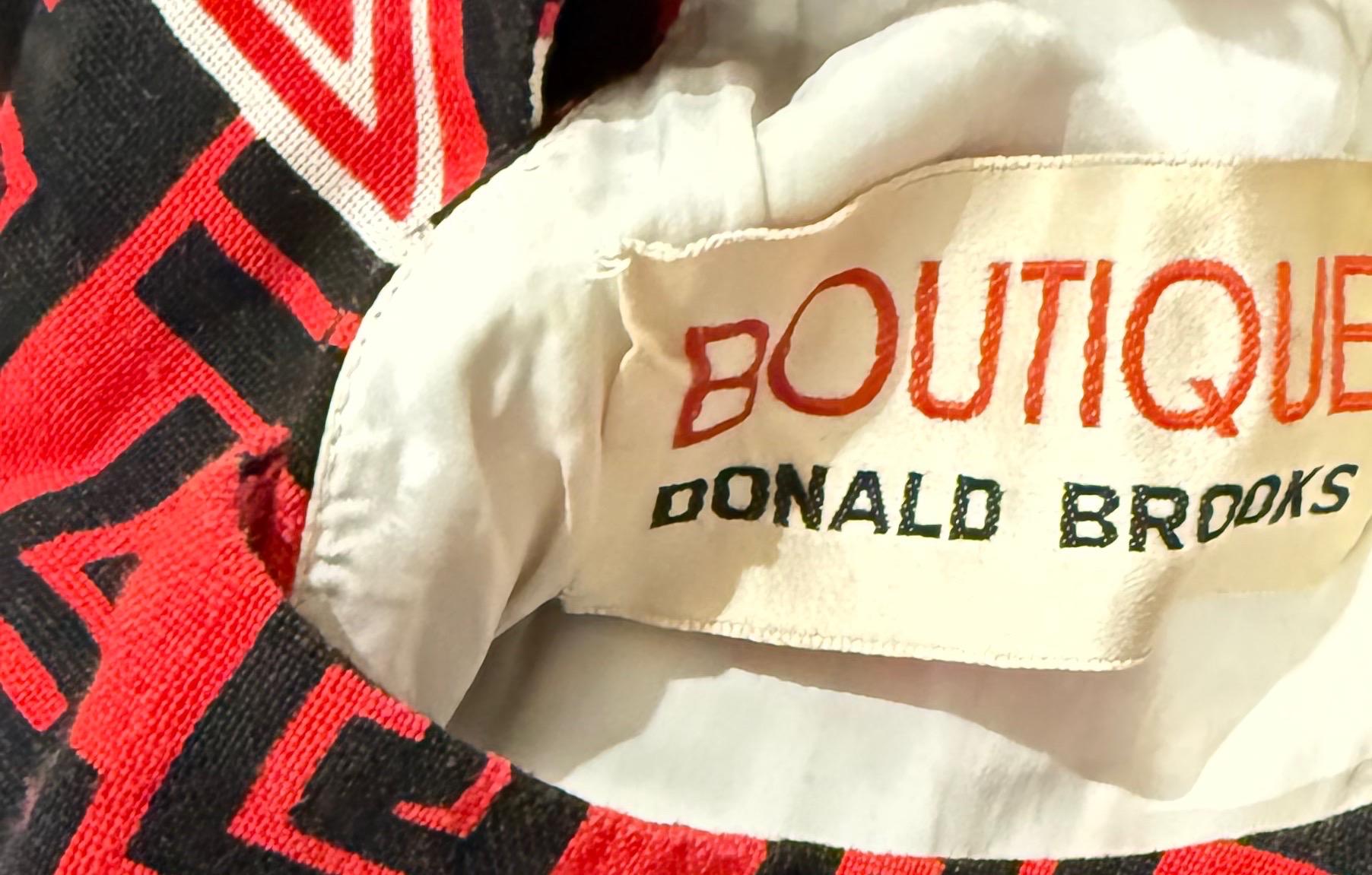 Step into the playful sophistication of 1960s American fashion with this striking Donald Brooks Boutique linen dress. Known for his modernist approach and witty prints, Donald Brooks delivers a conversation starter with this bold red, black, and