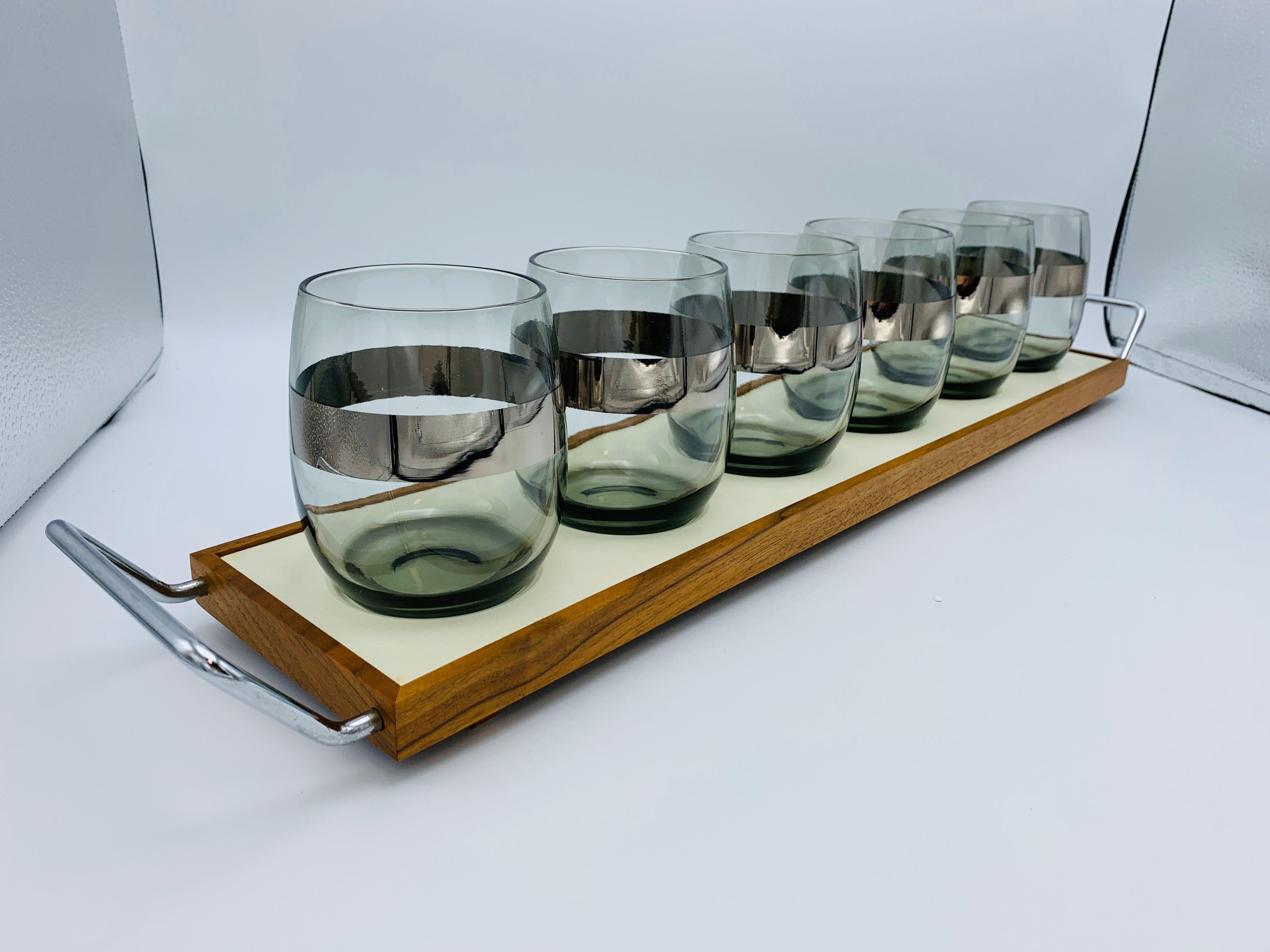Listed is a set of six, 1960s Dorothy Thorpe cocktail stemless wine glasses with a walnut tray. The glasses have Dorothy Thorpe's signature silver detailing stripe towards the center of the glass. The walnut wood has slim, chrome handles on two