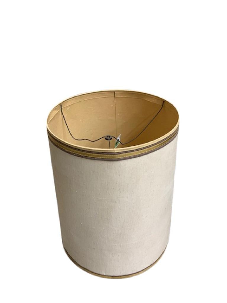 A linen drum-shaped lamp shade. Made of off-white linen with gold grosgrain ribbon trim on top and bottom edges, US, circa 1960.

Dimensions (in inches):
14” W x 19.25” H
16.5” shade holder drop from bottom of shade.
  