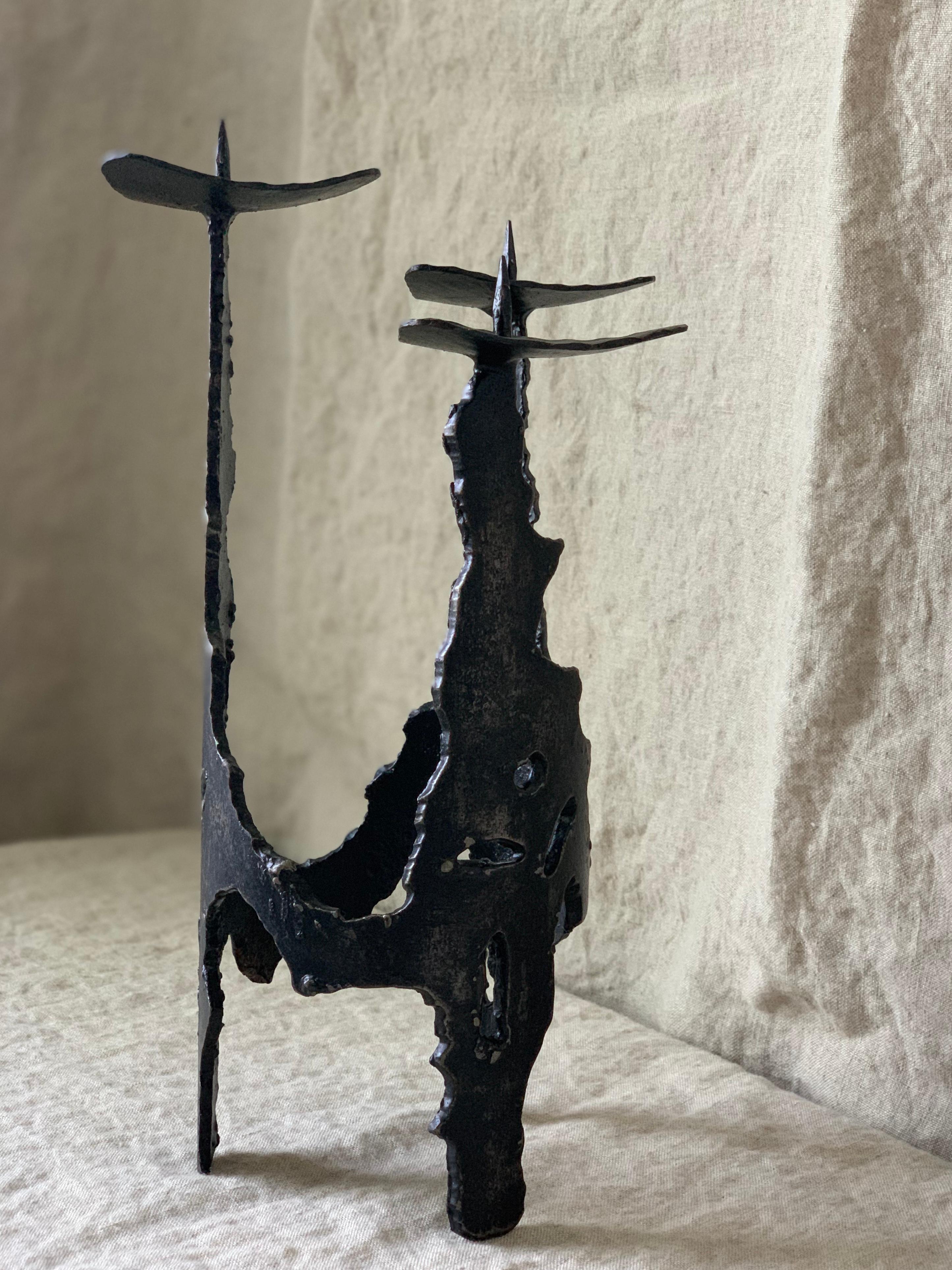 Wrought iron brutalist candle holder, handmade in former GDR . Tripod structure is carved in distinct brutalist aesthetic; roughly carved motifs. Candle rests are designed in a triangular fashion, resembling a flower petal. Highest point measures