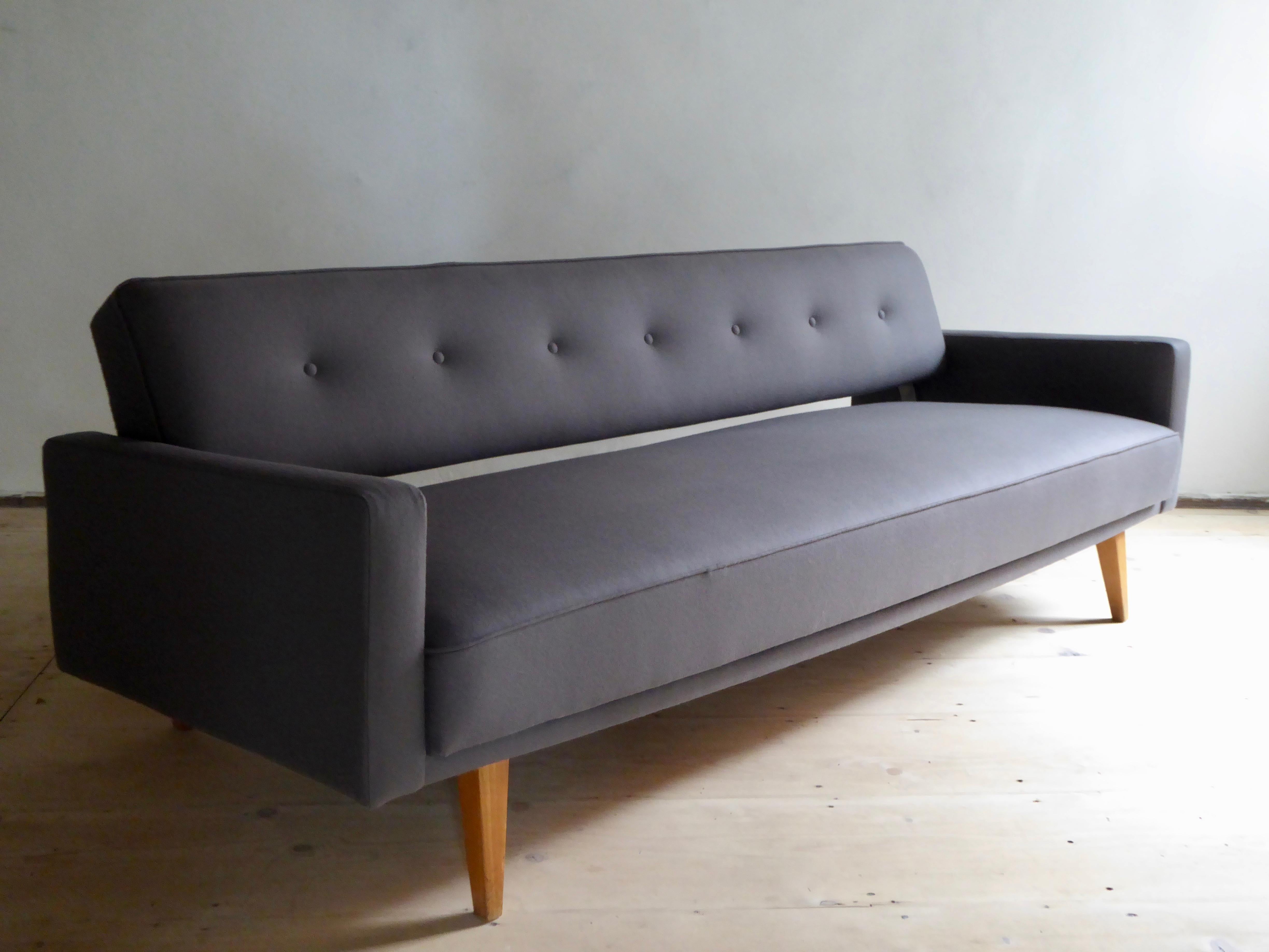 This straight line, minimalistic daybed is a beautiful and elegant sofa and a practicable and comfortable lounger with a simple handle. It is completely reupholstered and covered with a pure and smooth wool fabric in taupe of highest