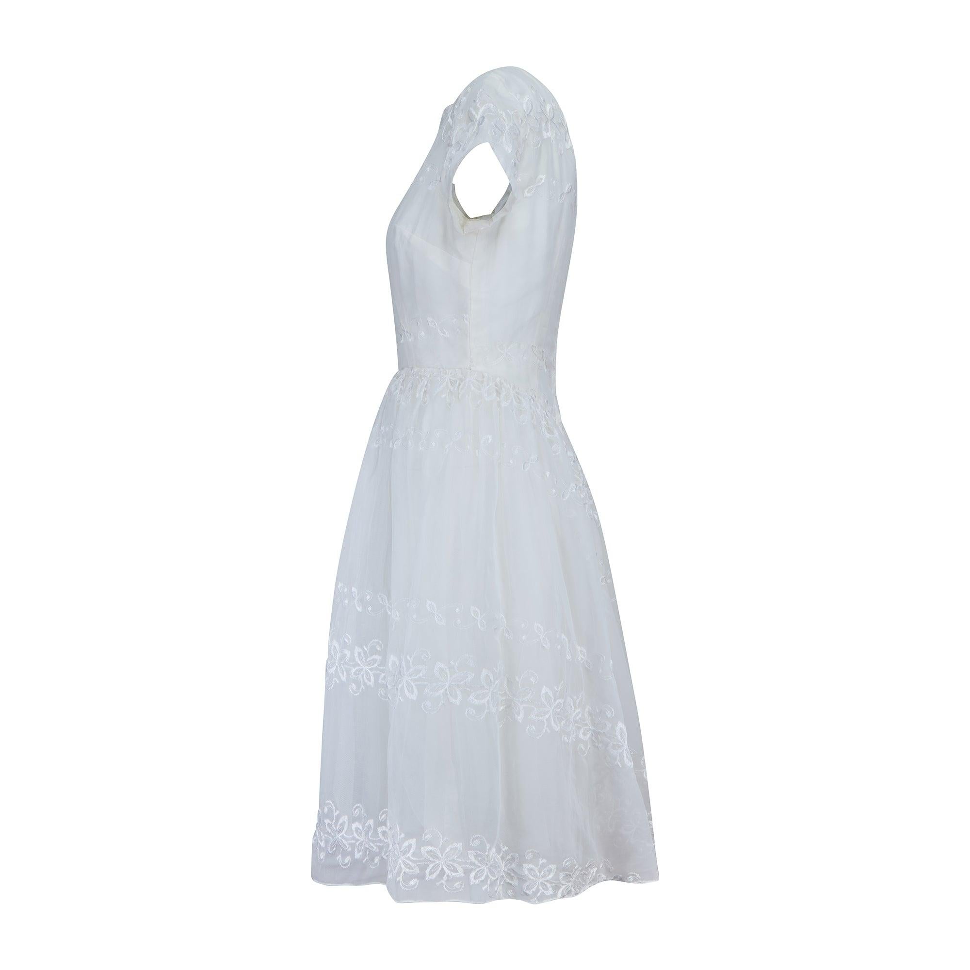 Cette douce robe à manches courtes a été créée par un designer inconnu dans les années 1960 et pourrait avoir été une robe de mariée, car elle est d'une délicate nuance de blanc. Elle est confectionnée en mousseline de soie synthétique brodée à la