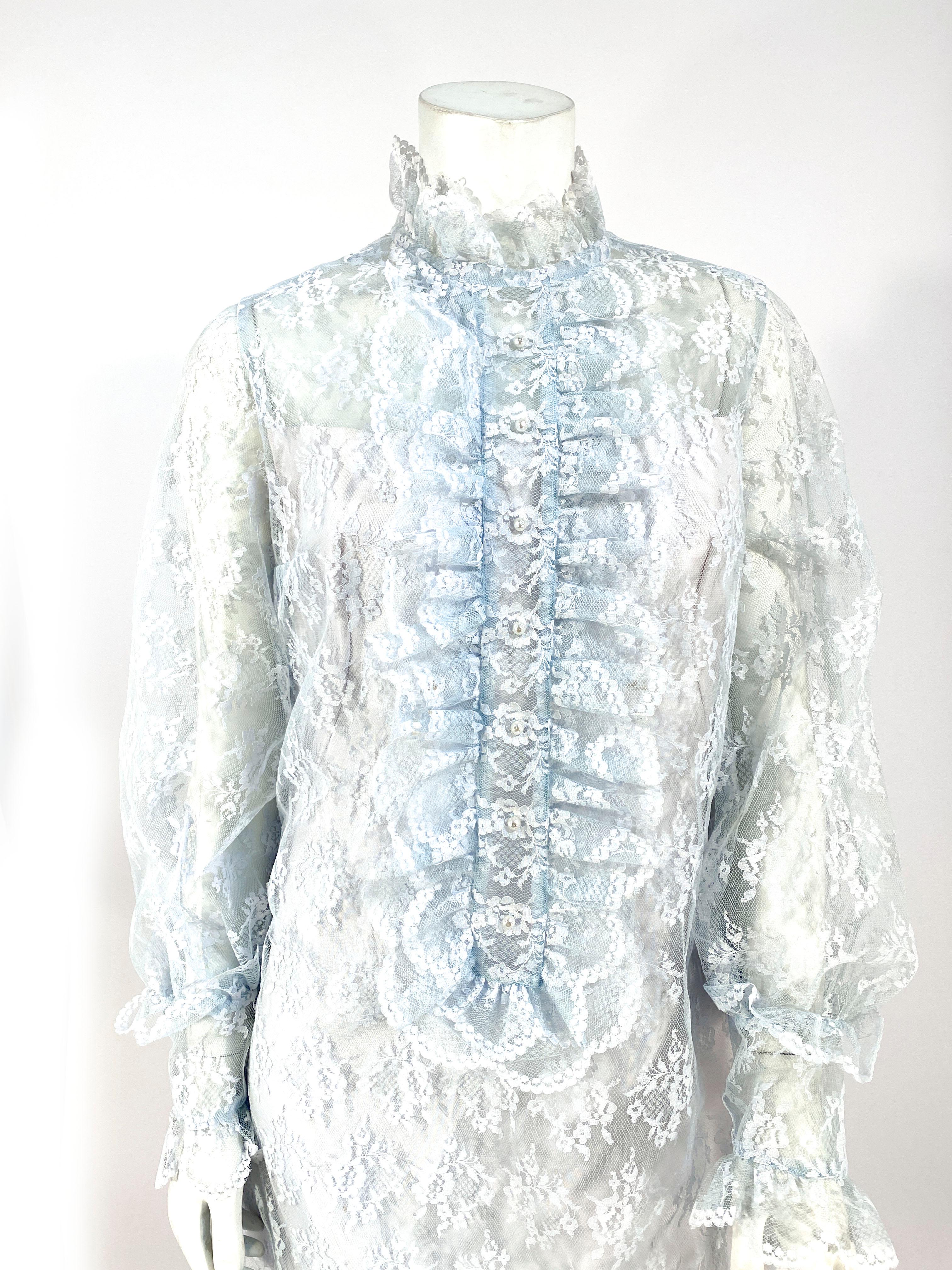 1960s Emma Domb shift dress made of a powder blue floral lace and a twill fitted lining. The face of the dress is decorated with an Edwardian-style attached jabot, high neck, and pearl buttons. The long sheer sleeves are finished with