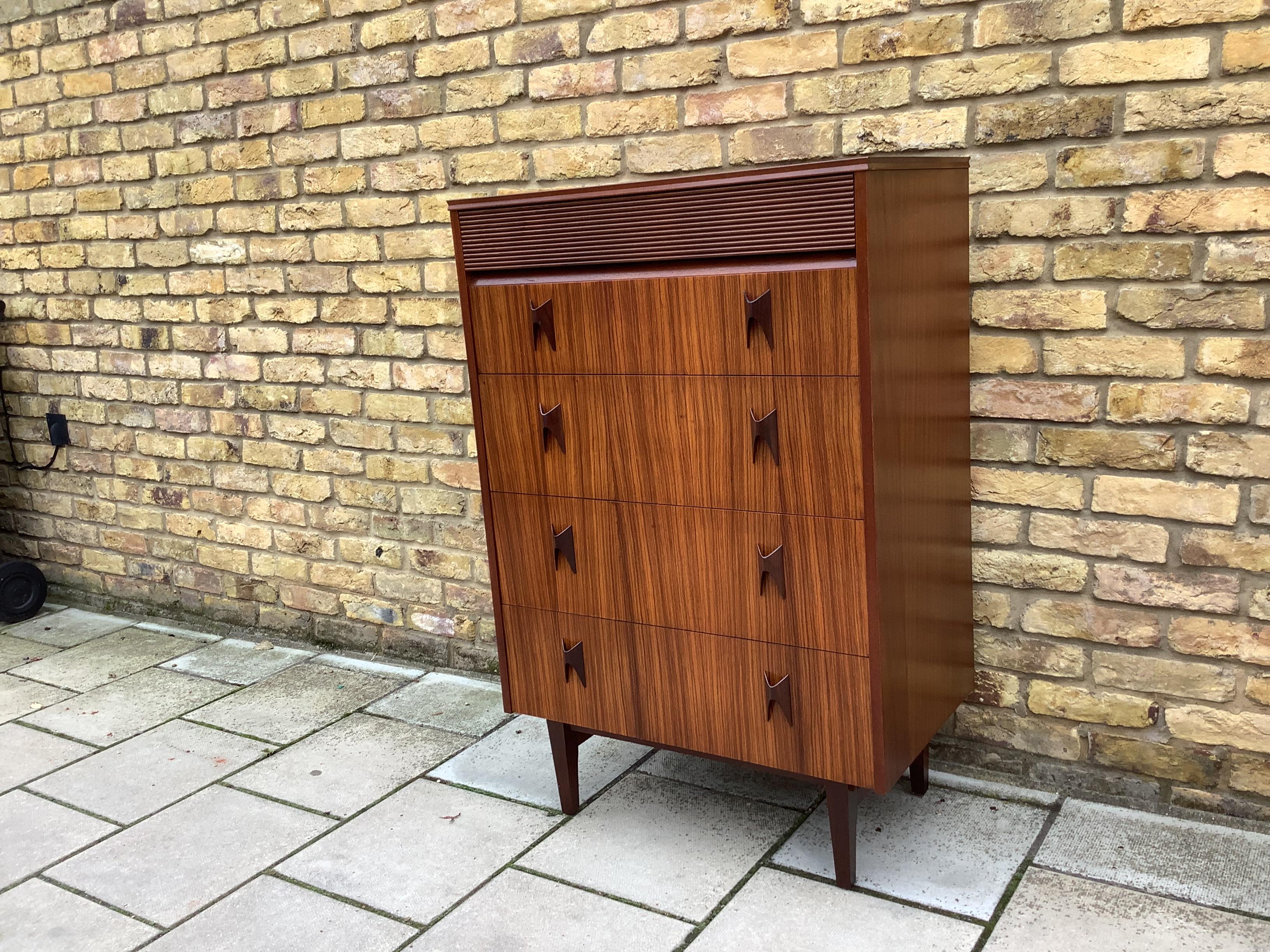 A rare beautiful and very well made vintage chest of drawers, this was made by Elliots of Newbury in the 1960’s. It is made from a fantastic combination of woods, with zebrano drawer fronts, rosewood handles and a walnut frame


Measures: Width –