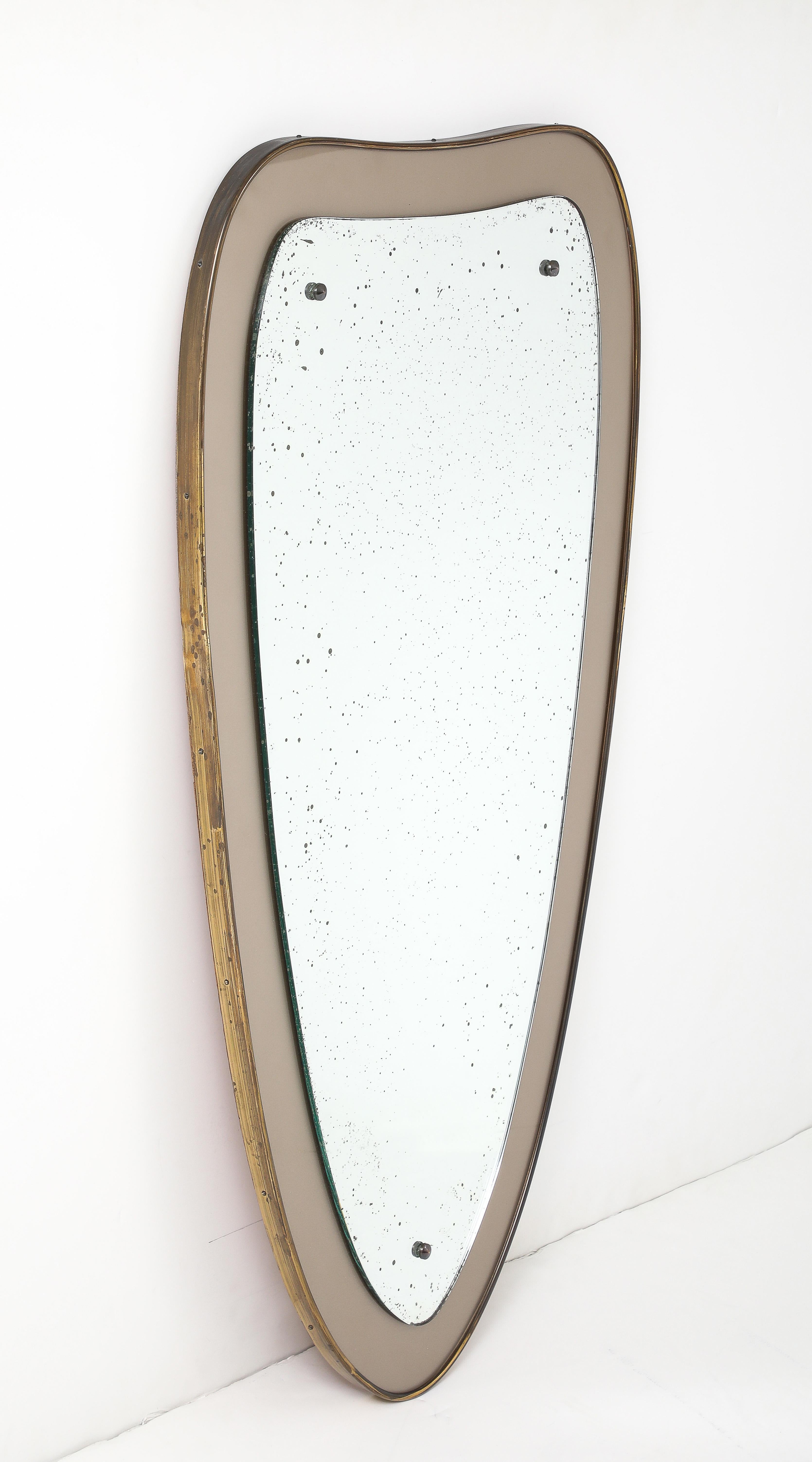Specchio da parete in ottone patinato della metà del secolo scorso, attribuito a Ettore Sottsass, in condizioni originali d'epoca con alcuni segni di usura e patina sull'ottone e sullo specchio dovuti all'età e all'uso. 