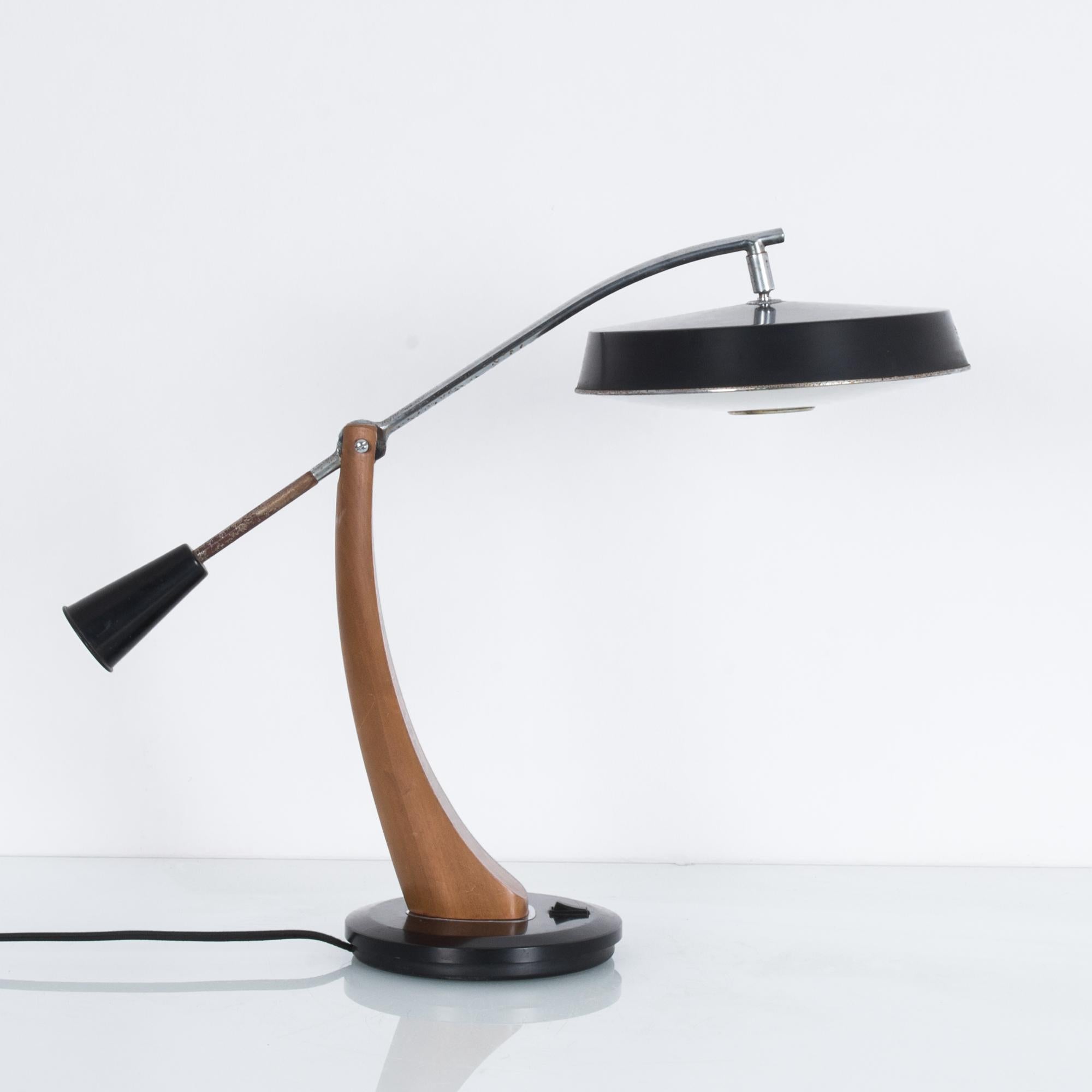 A pendulum desk lamp made by Spanish designers Fase President. A curved wooden arm with a counterpoised metal rod supports a black lacquered lampshade while allowing the bulb to be raised and lowered. The convex, gently frosted lower disc of the