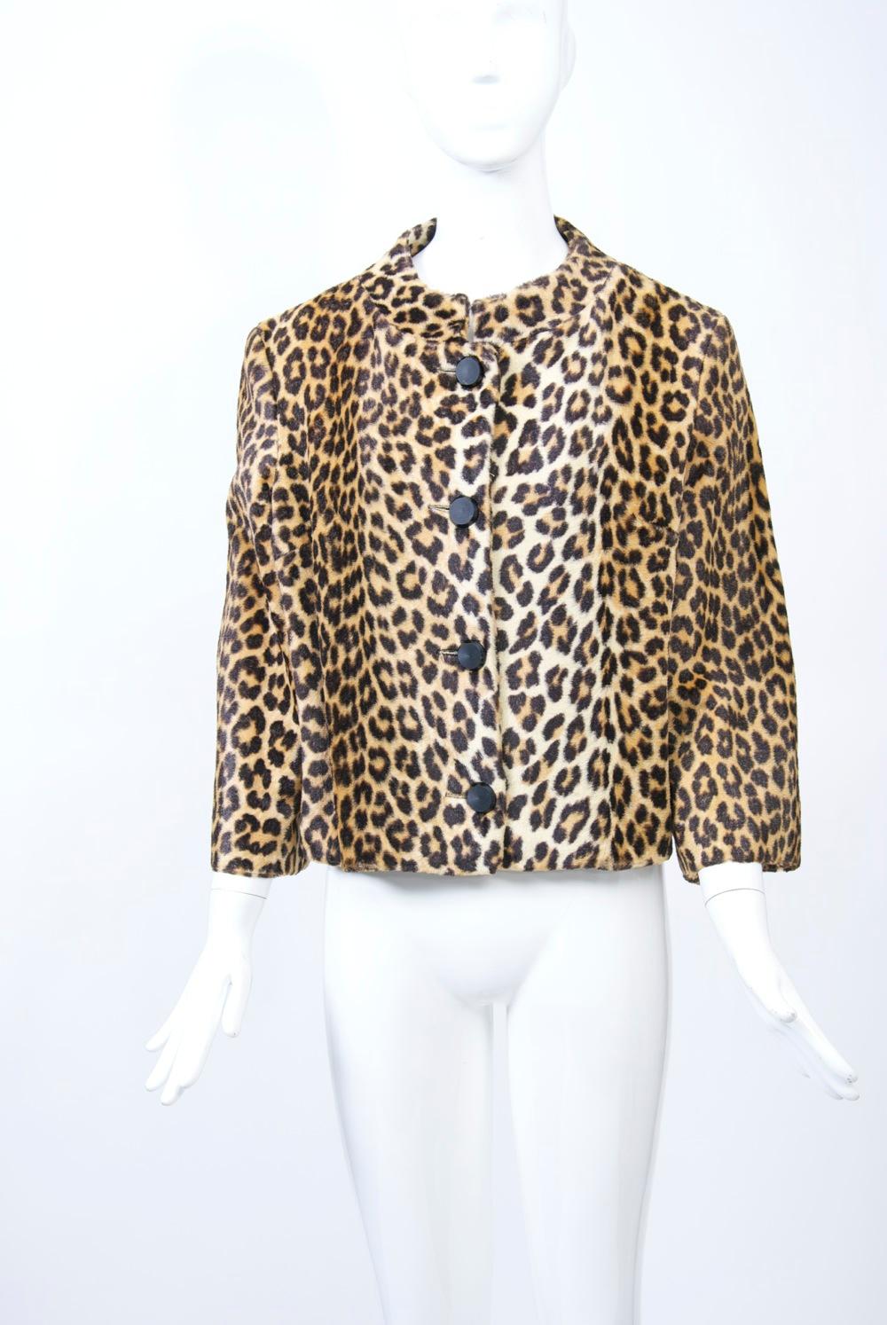 1960s cropped jacket in faux leopard skin features a low stand-up collar and above-the-wrist sleeves. Four black buttons close the single-breasted jacket. Black lining. Approximate size 6-8. Made for and retailed by New York department store