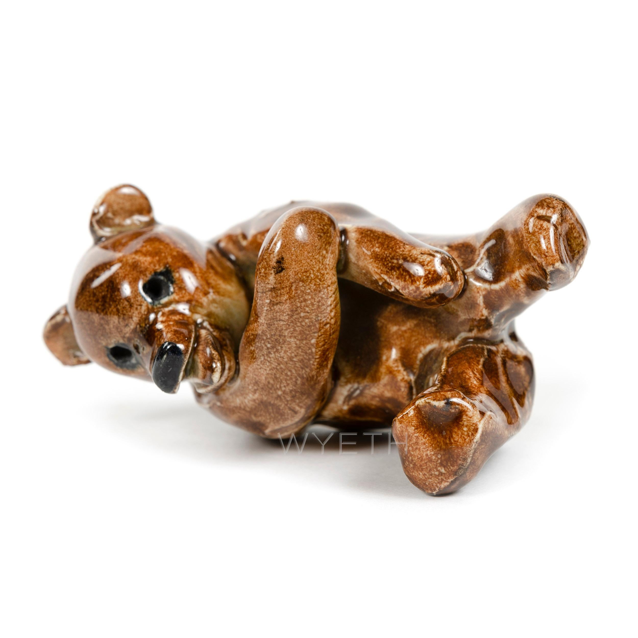 A cheerful and small ceramic bear laying on its back, laughing, in a high-gloss brown and black glaze.
