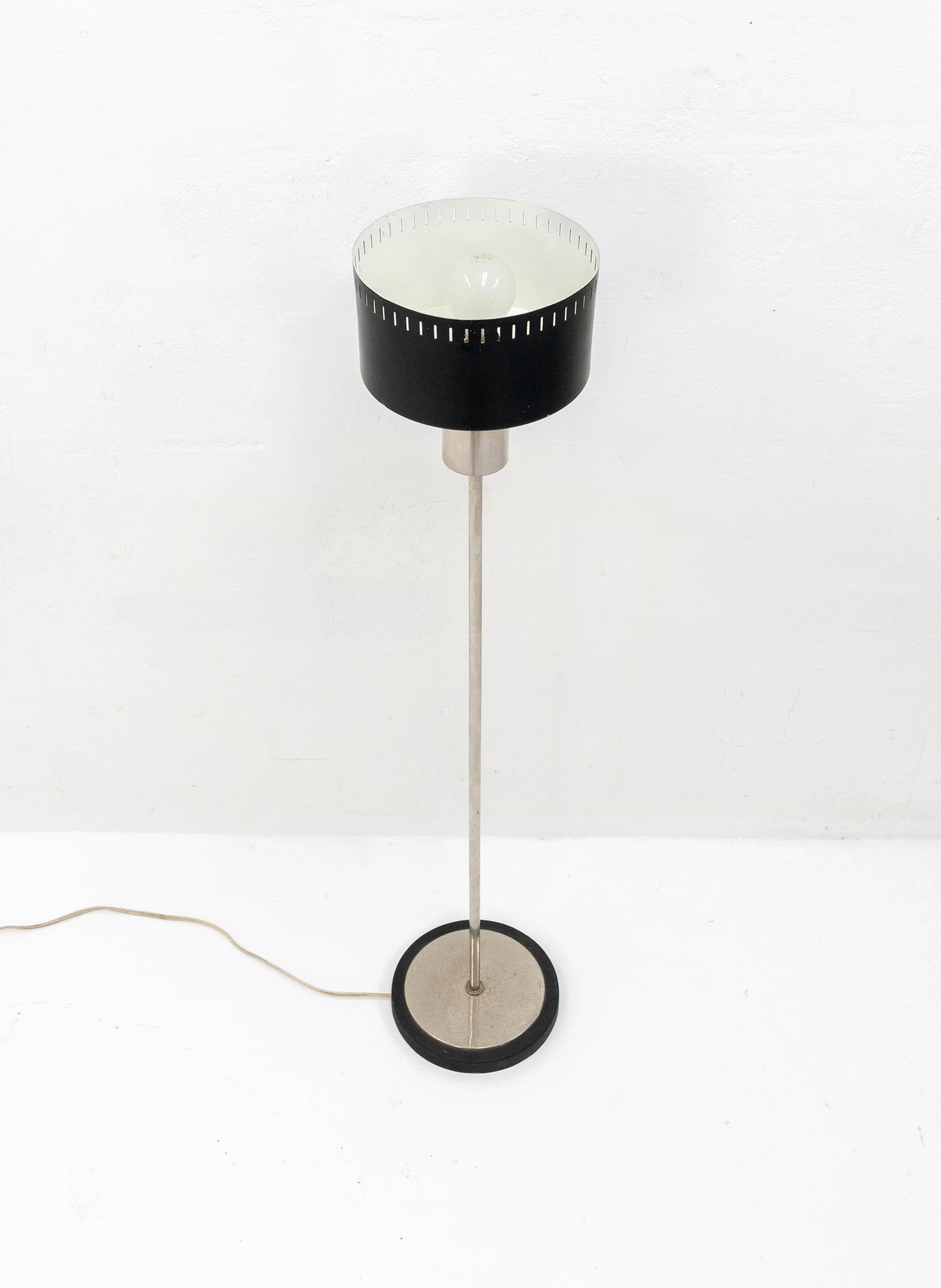 Small elegant floor lamp in a style reminiscent of Stilnovo examples. Chrome base with a black metal lampshade featuring a slotted design. The height makes it suitable for use as a reading lamp next to a chair or desk.