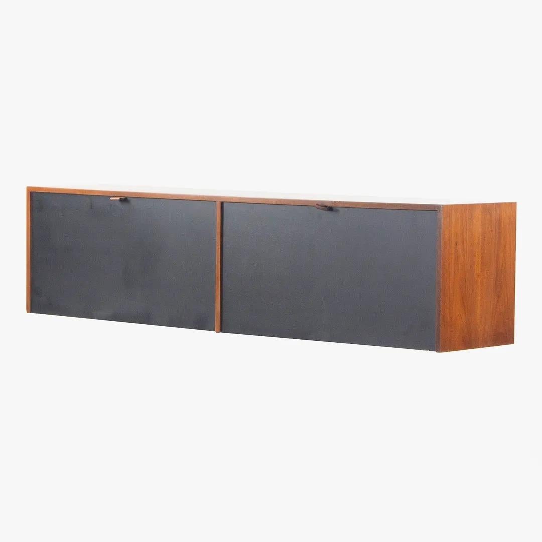 Listed for sale is a gorgeous 1960s walnut wall-mounted hanging cabinet with leather pulls and contrasting black doors, produced by Knoll Associates and designed by Florence Knoll. This example is in fantastic shape with original hardware. The