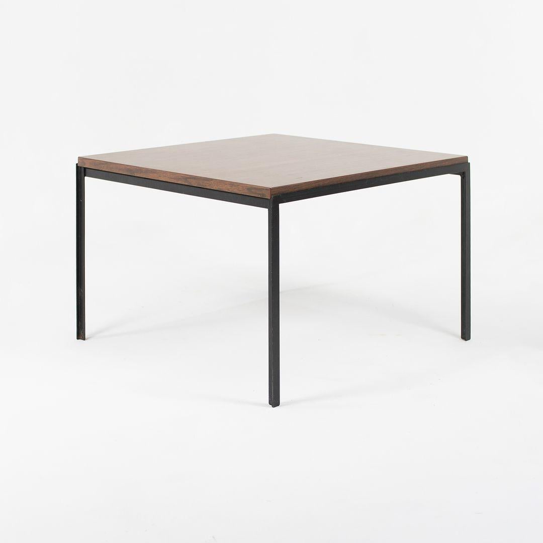 Il s'agit d'une table d'appoint à angle droit Florence Knoll, modèle 304, conçue à l'origine en 1952. Il présente un plateau carré avec une surface en stratifié (formica) grain de bois noyer et des pieds en acier émaillé noir. Cet exemple