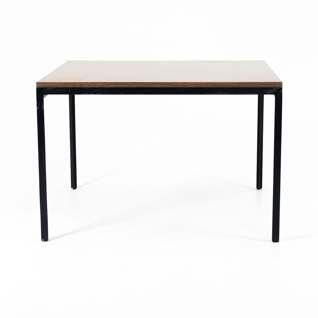 This is a Florence Knoll T-Angle Coffee Table, initially designed by Florence Knoll for Knoll Associates in 1952. This example dates to the 1960s. It features a square top with a brown faux-woodgrain laminate surface, and has black enameled-steel