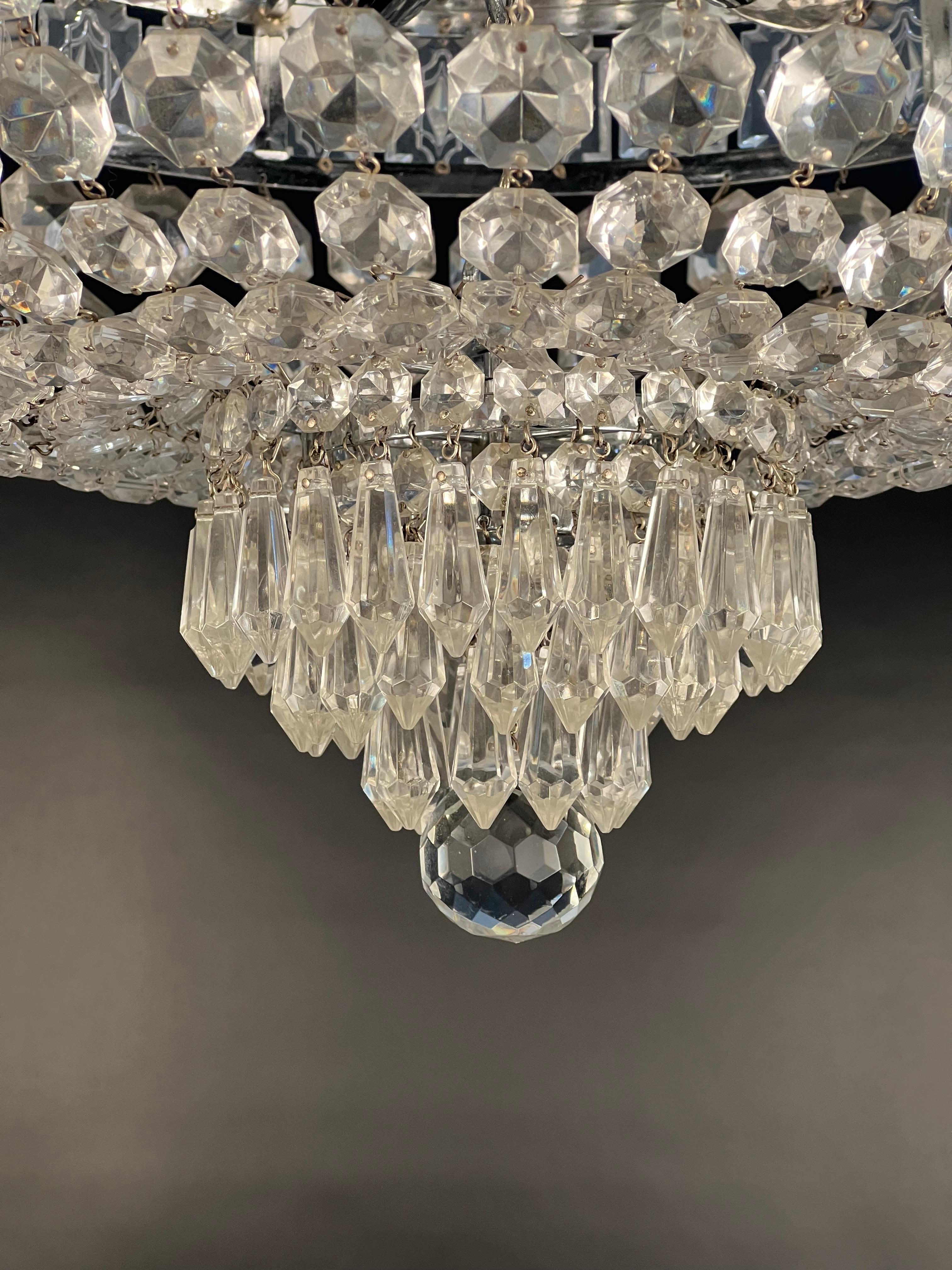 An empire style semi flush mount crystal basket featuring a central band of rectangular flat crystals with arched edges and etched design within the field. From the central band are graduating jewels leading to a three-tiered cluster of faceted
