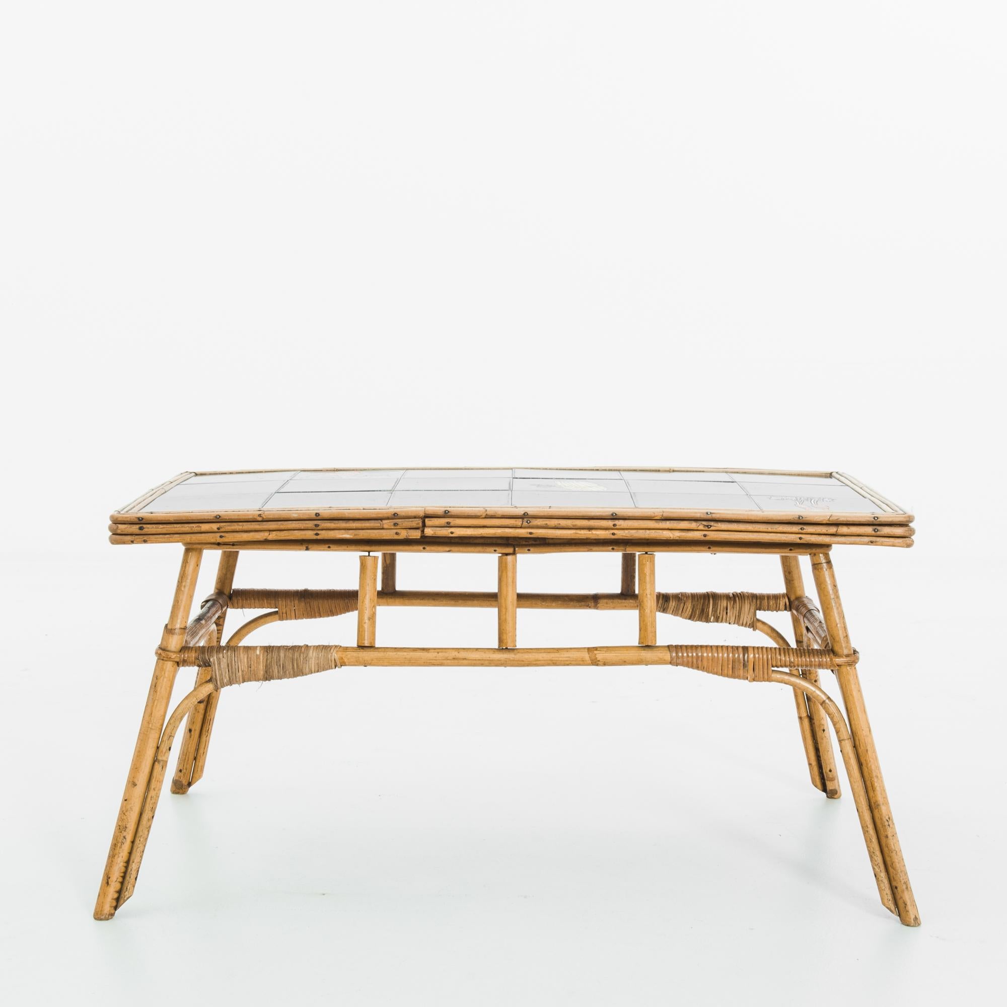 A bamboo coffee table from 1960s France, with a tiled top. The bamboo frame is light and angular, with a pleasing warm patina. Black ceramic tiles, punctuated with graphic red, green and yellow motifs — a pair of radishes, a bunch of asparagus,