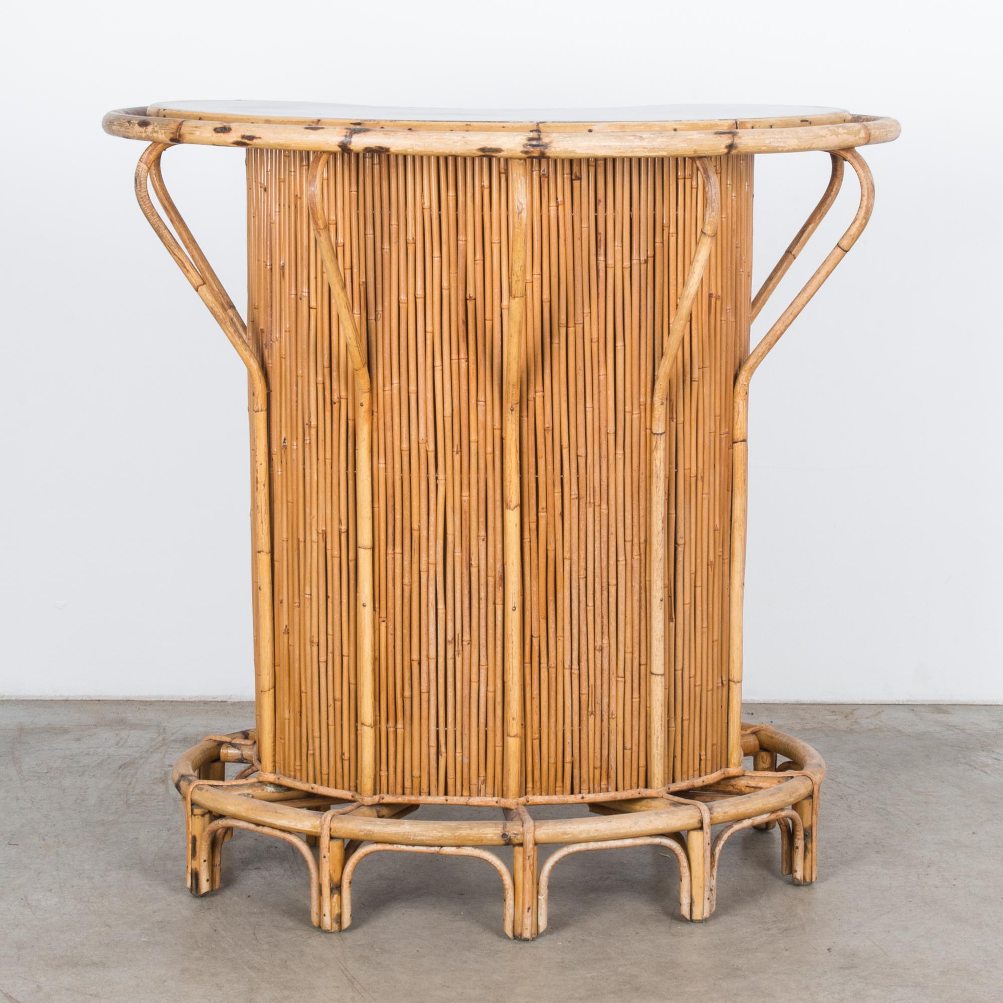 This dry bar was made in France, circa 1960 from bamboo. The curved arms and circular platform accentuate the distinctive bean shape construction, which houses three shelves painted black.