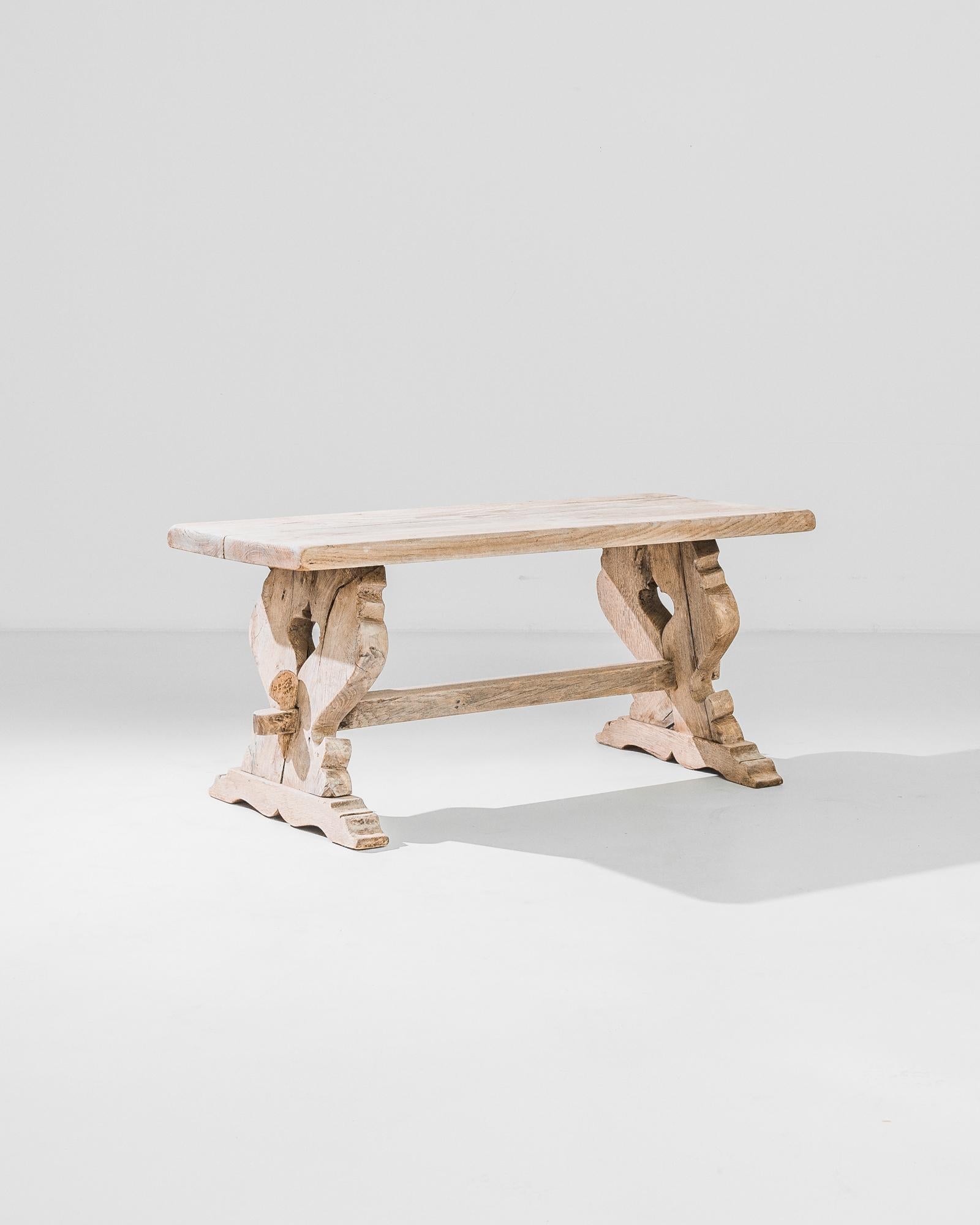 A bleached oak coffee table from France, produced circa 1960. Two gently angled, heart shaped legs connected by a simple stretcher rendered in a bright oak, make for a charming coffee table. A modern table with significant French country style