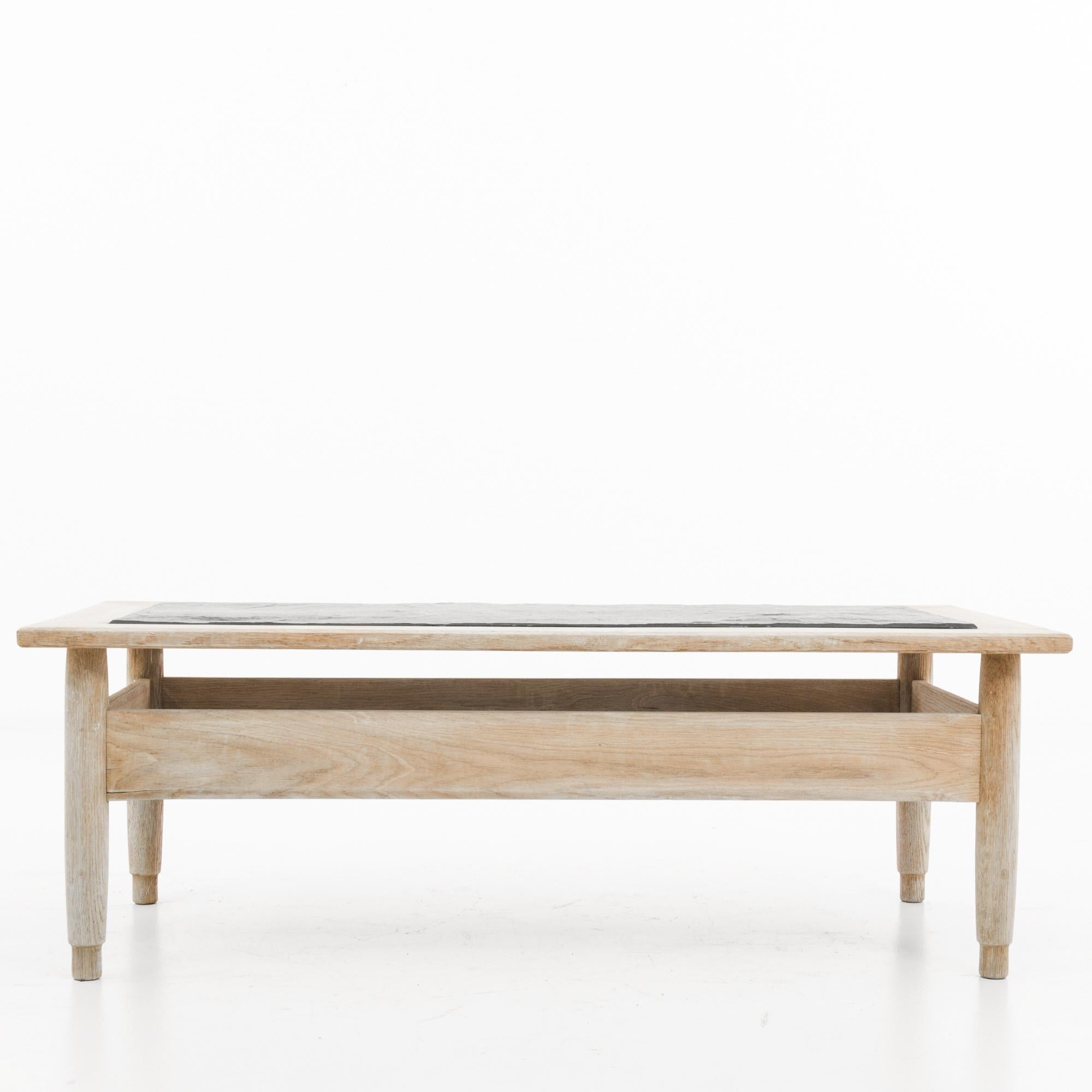 A bleached oak table with stone top produced in France in the 1960s. Low-slung coffee table in the rustic vein of the mid-century modern with its simple silhouette, wide stretchers, and organic feeling bevel as legs turn to feet. The black stone