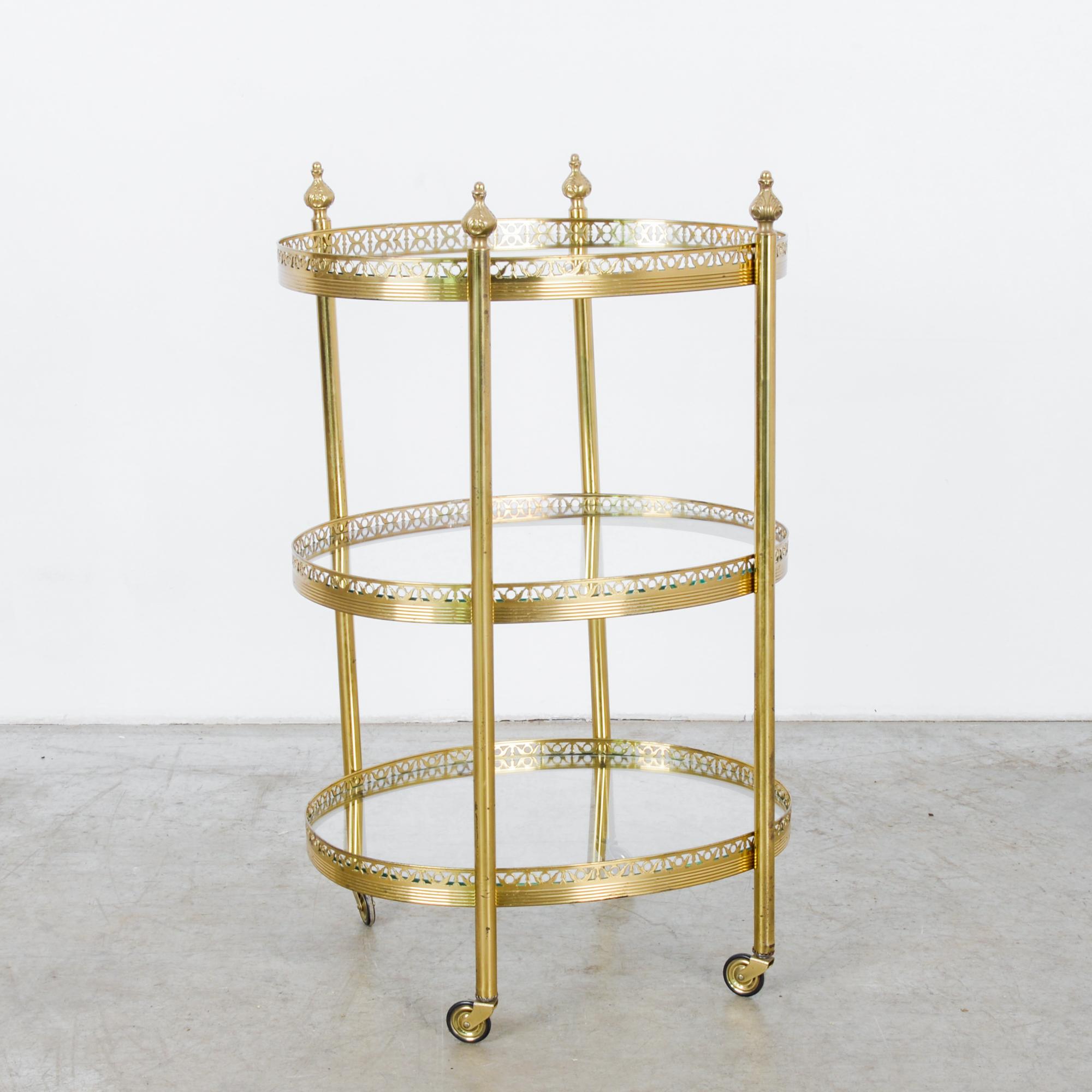 A vintage brass bar cart on wheels from France, circa 1960. Three tiers of ovoid glass shelves ringed by avian motif in silhouette. Four slender legs capped by budding petals support the delicate body of this charming cart. Plenty of space to hold