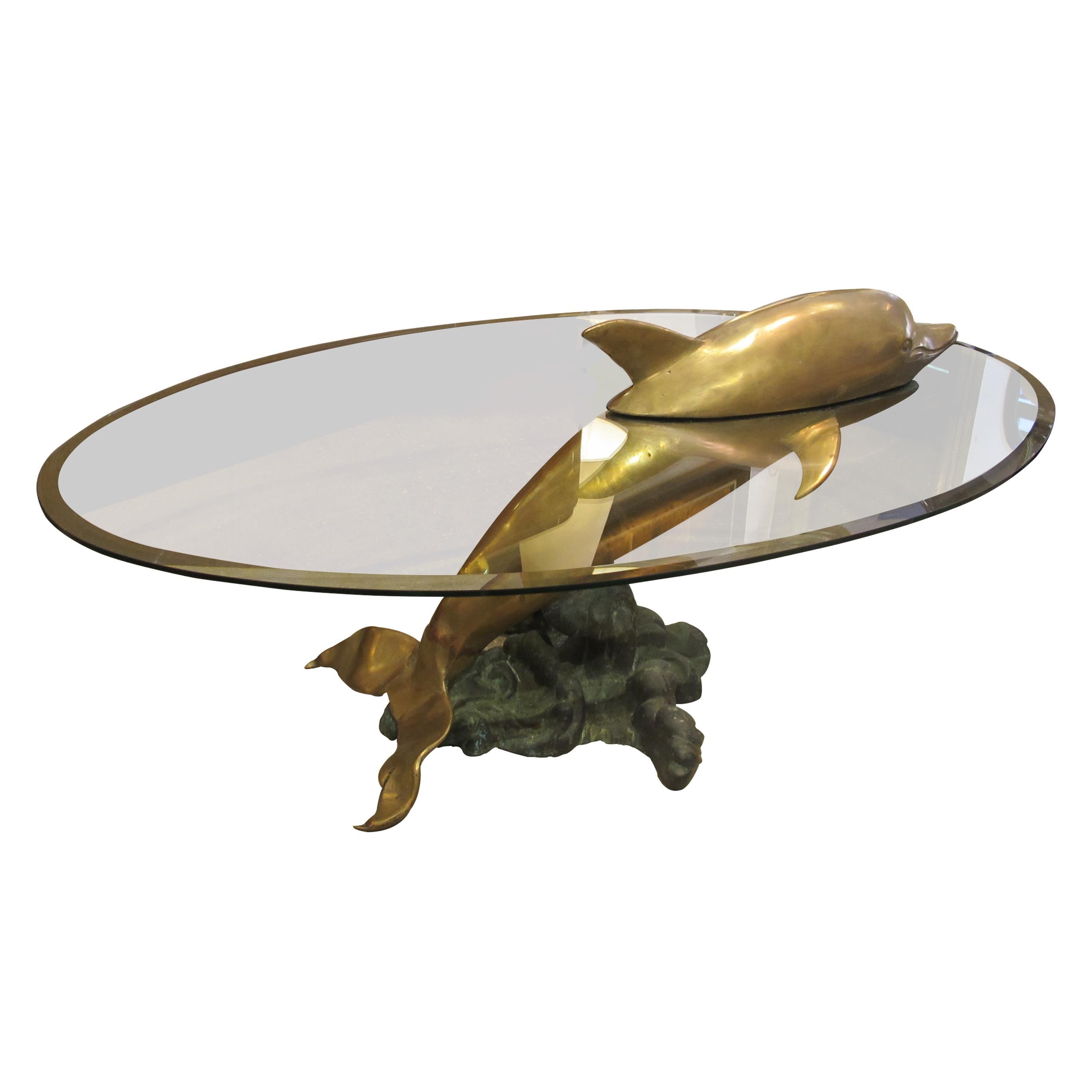 1960s coffee table with a brass dolphin sculpture bursting through the original oval bevelled glass top which effortlessly combines functionality and artistry. At the heart of this coffee table stands a meticulously crafted brass dolphin, skilfully
