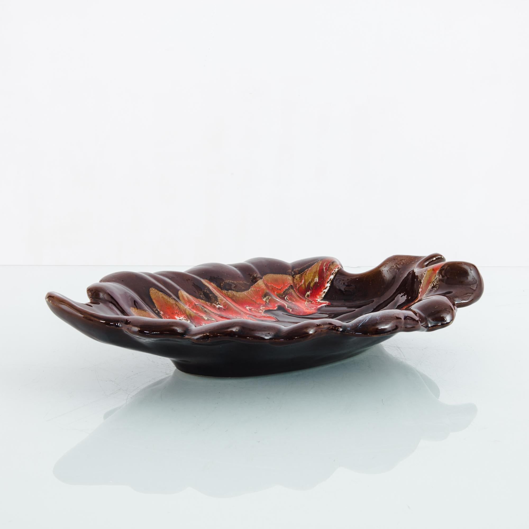 This ceramic bowl was made in France, circa 1960. Crafted with waves that rise on the sides, the bowl resembles a leaf with curled edges. A captivating vintage piece with a rich burnt sienna glaze and a flaming lake of red, ochre, and white within.