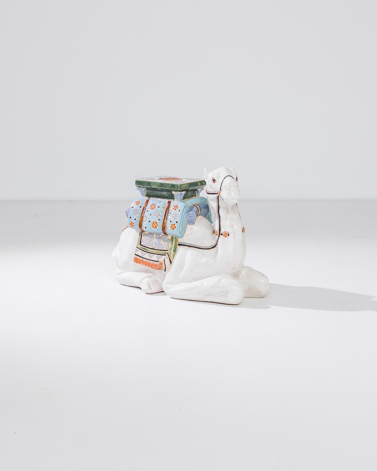 A ceramic decoration from 1960s France in the shape of a white camel. A rug, saddle and saddlebags are glazed with bright colors; the assortment of delicate patterns — reflecting Chinese and Arabic influences — suggest the romance of the Silk Road.