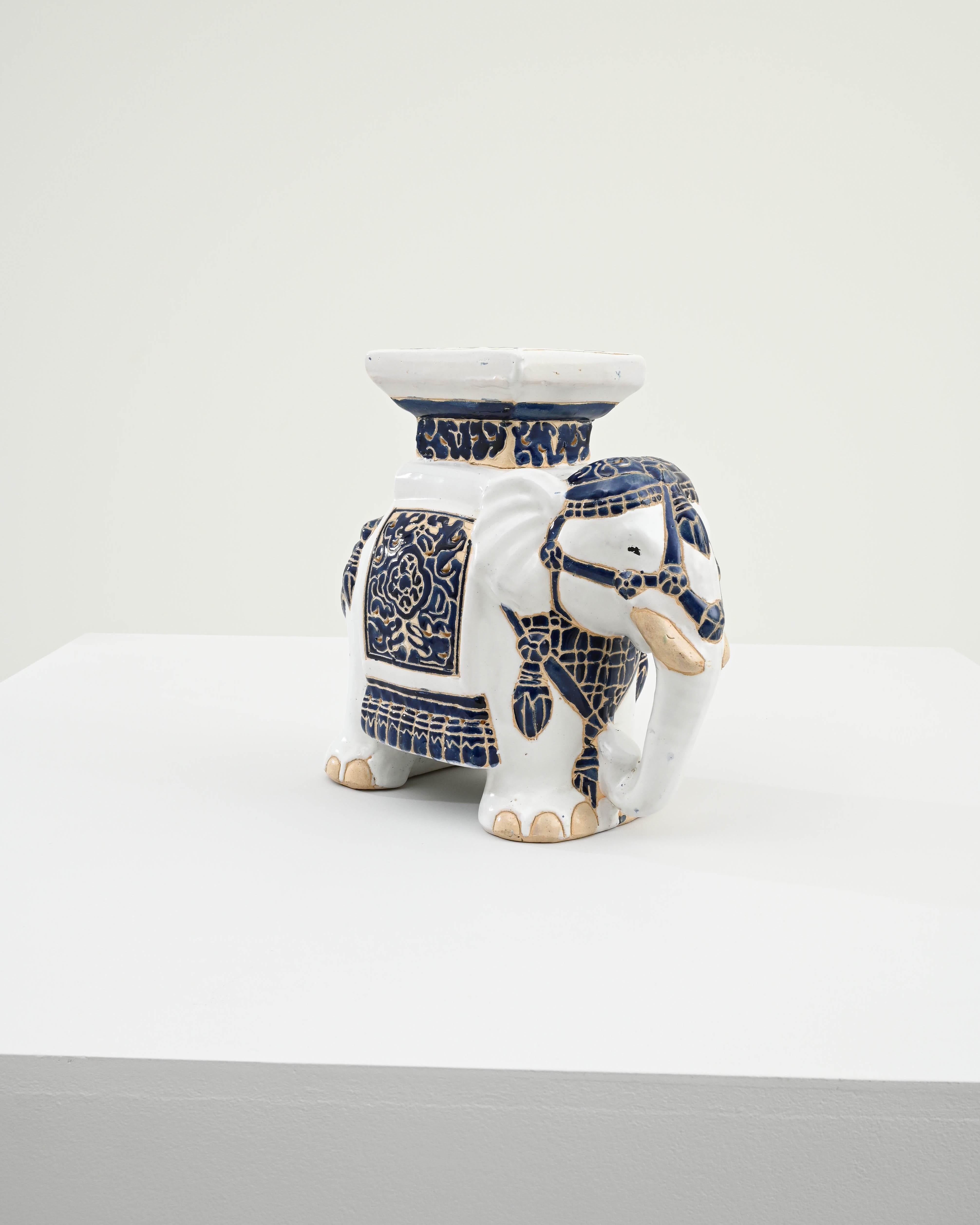A ceramic decoration from 1960s France in the shape of an elephant. A saddle seat and blanket are glazed with indigo blue, the elephant’s skin painted with glossy white and laced with lines of the earth tone clay body; the assortment of delicate