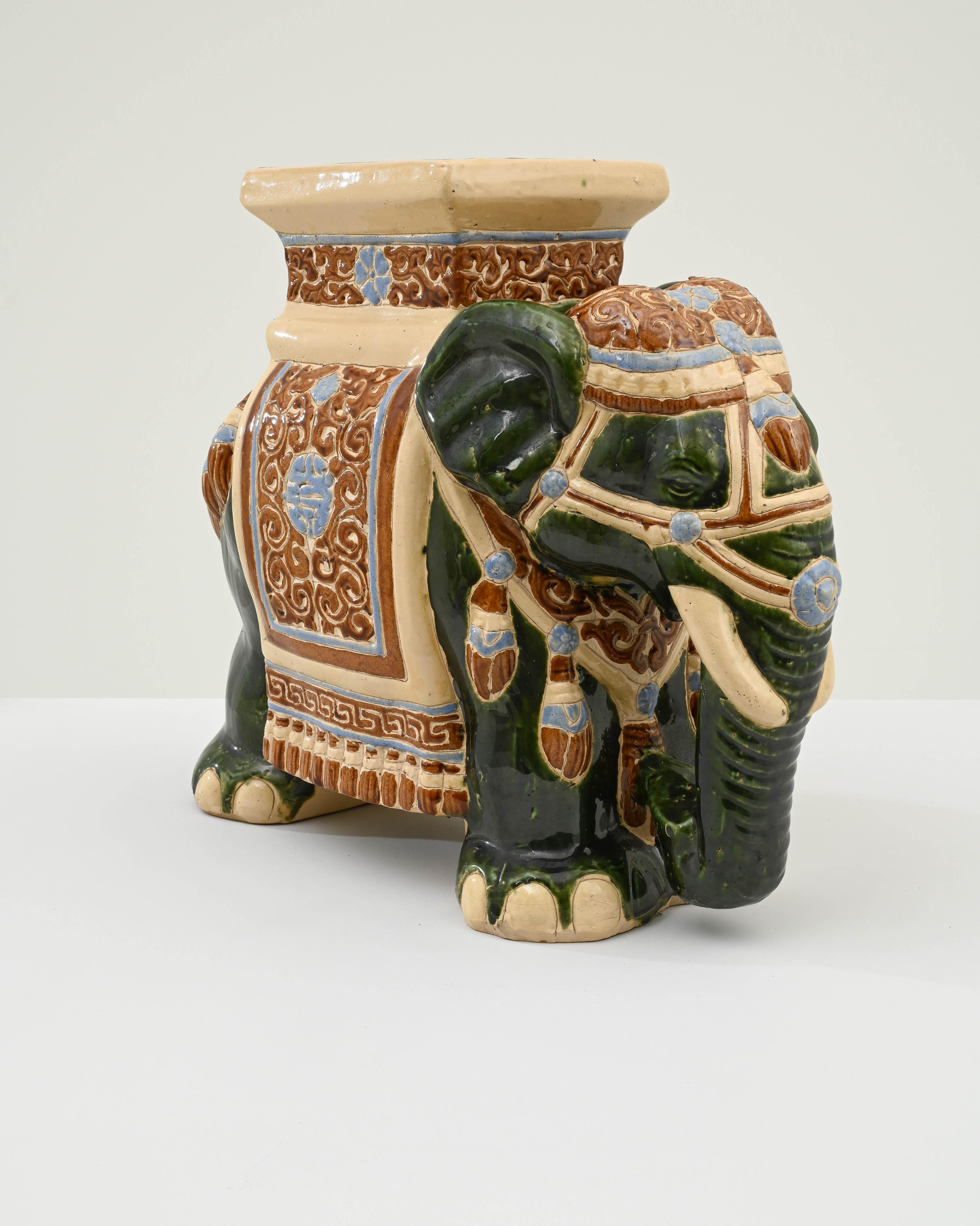 A ceramic decoration from 1960s France in the shape of an elephant. A saddle seat and blanket are glazed with pale blue and ochre, the elephant’s skin painted with dark celadon and laced with lines of the earth tone clay body; the assortment of