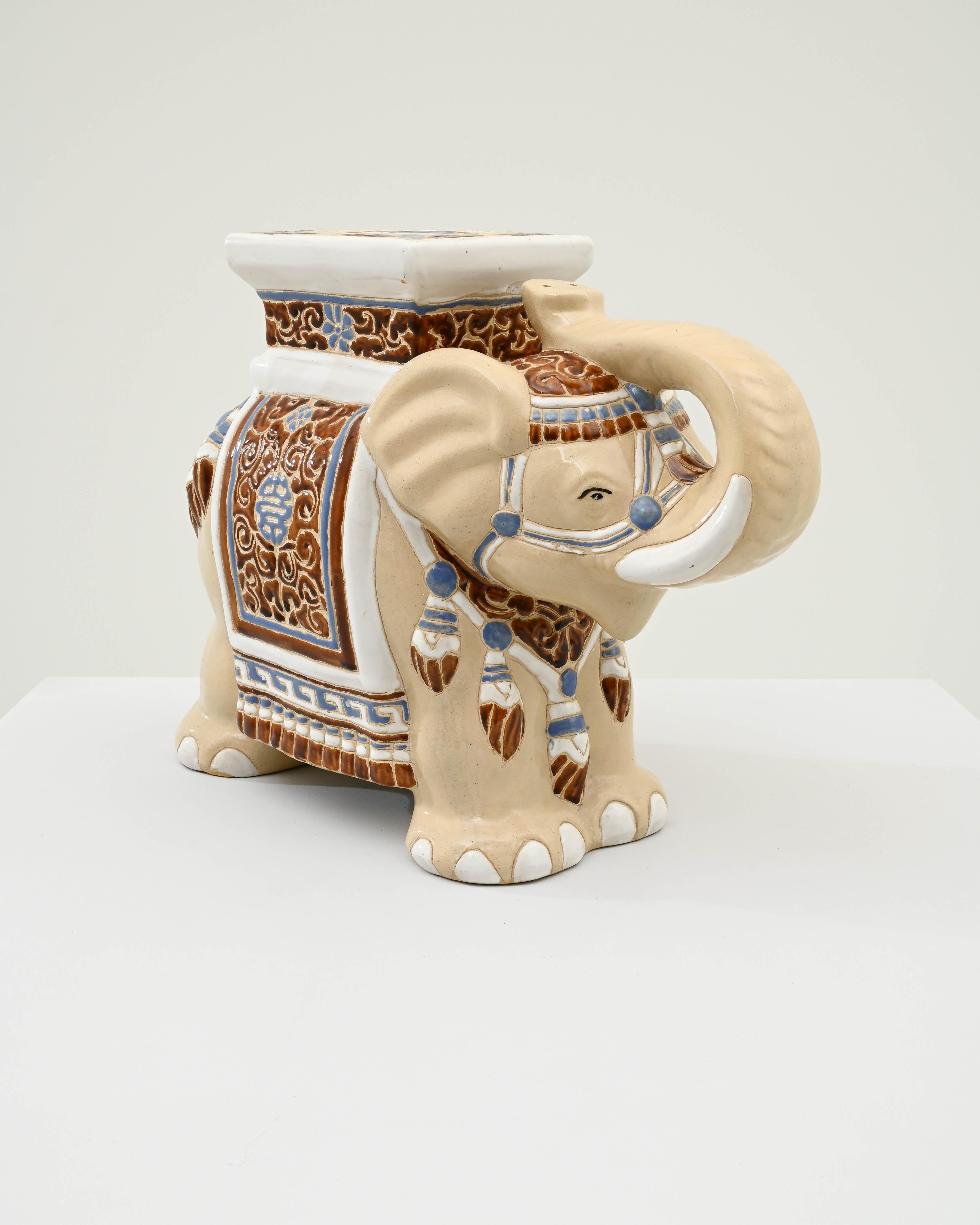 A ceramic decoration from 1960s France in the shape of an elephant. A saddle seat and blanket are glazed with pale blue and ochre, the elephant’s skin painted creamy off-white and laced with lines of the earth tone clay body; the assortment of