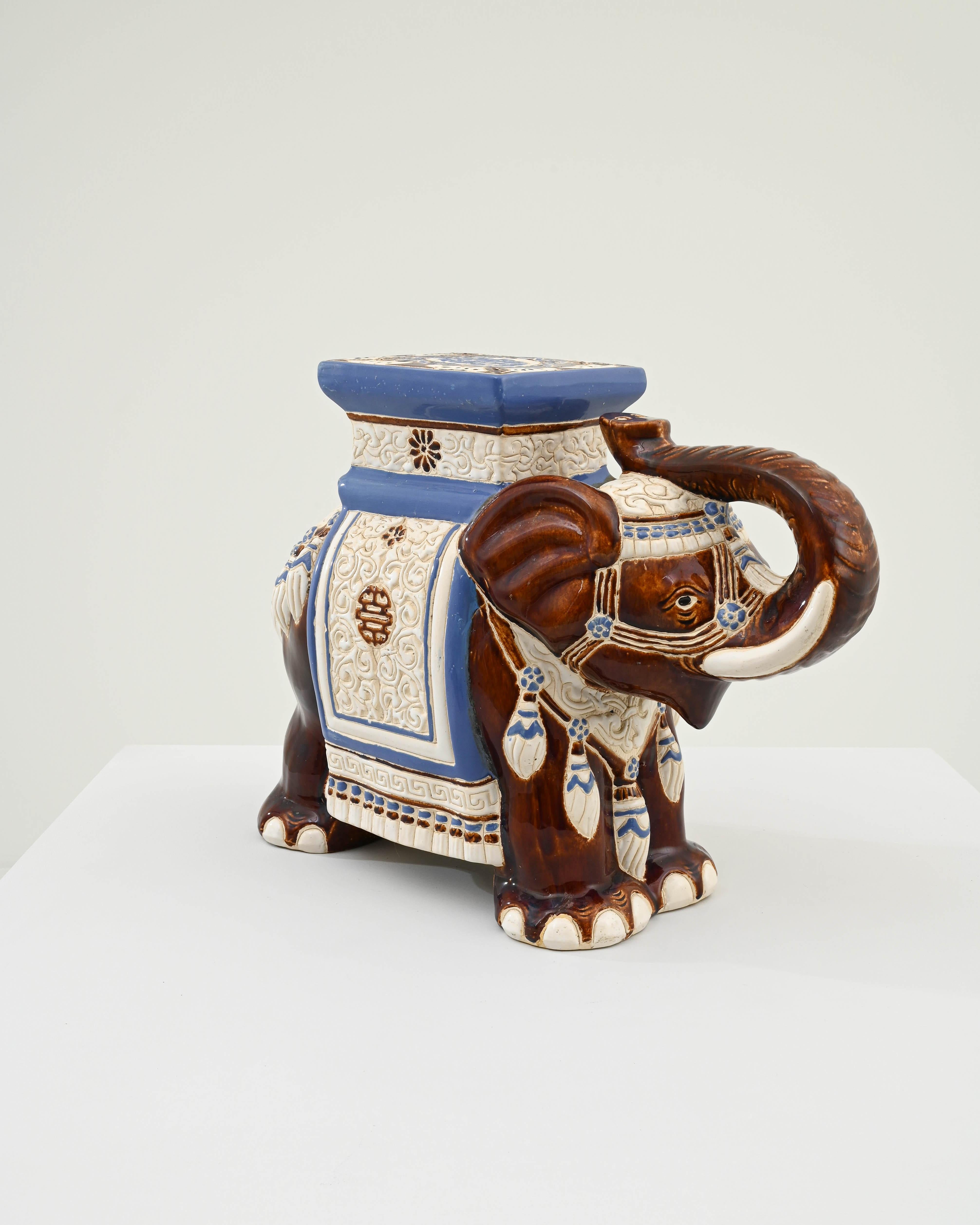 A ceramic decoration from 1960s France in the shape of an elephant. A saddle seat and blanket are glazed with pale blue and white, the elephant’s skin painted a rich burnt umber and laced with lines of the earth tone clay body; the assortment of