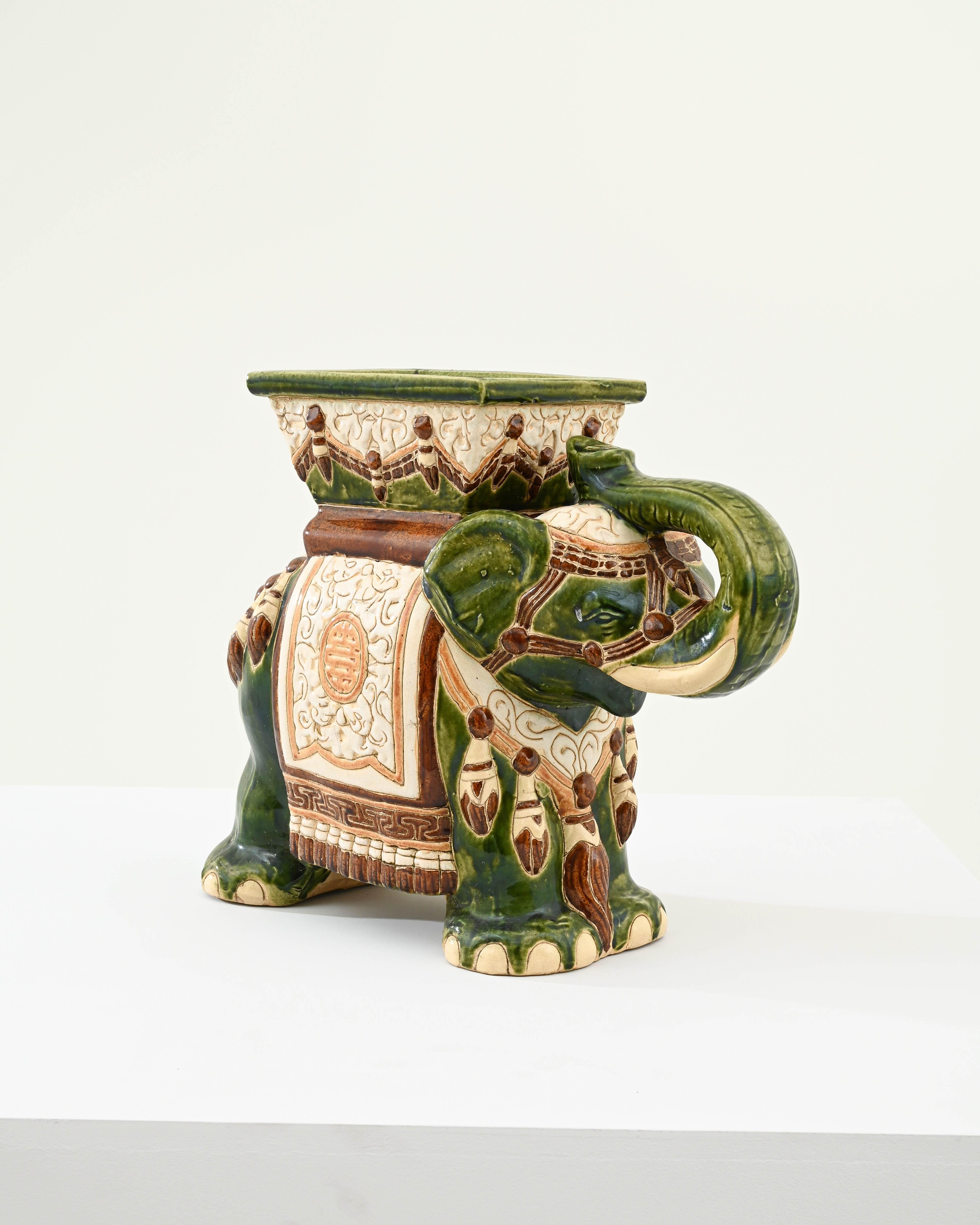 A ceramic decoration from 1960s France in the shape of an elephant. A saddle seat and blanket are glazed with ochre and white, the elephant’s skin glinting a fern-like jade and laced with lines of the earth tone clay body; the assortment of delicate