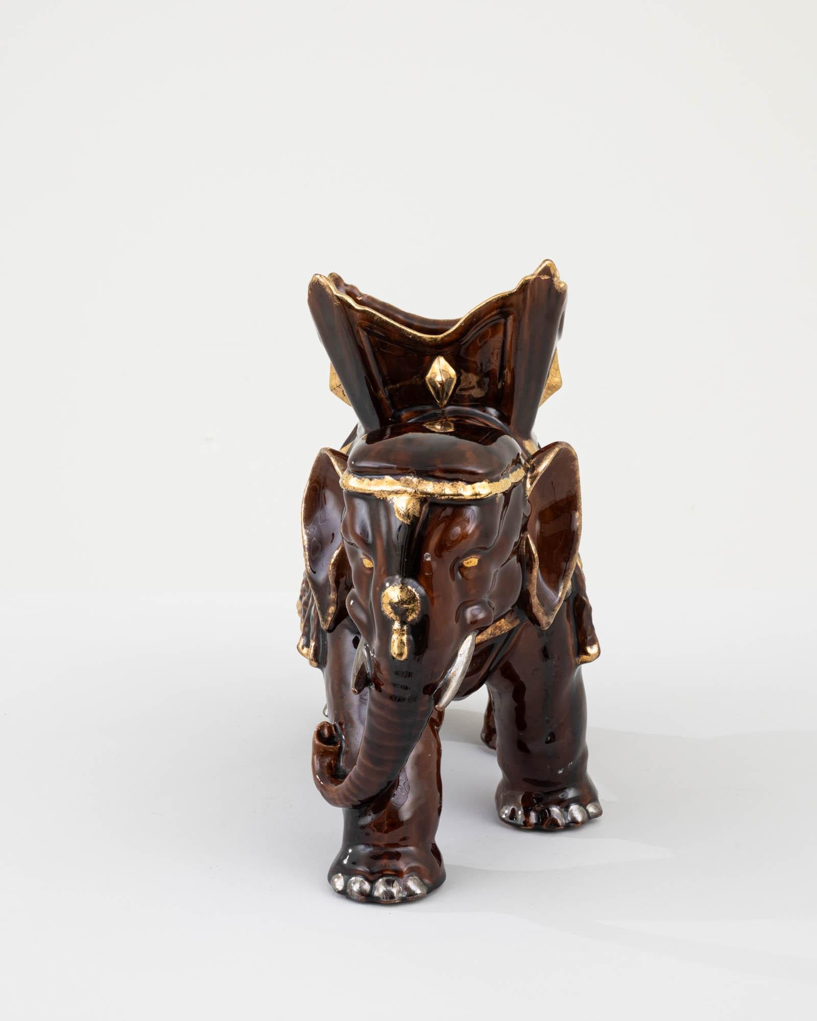 Step into the realm of vintage elegance with this exquisite 1960s French Ceramic Elephant, a true testament to mid-century artistry. This charming figurine showcases a rich, glossy chestnut glaze, complemented by opulent gold accents that highlight