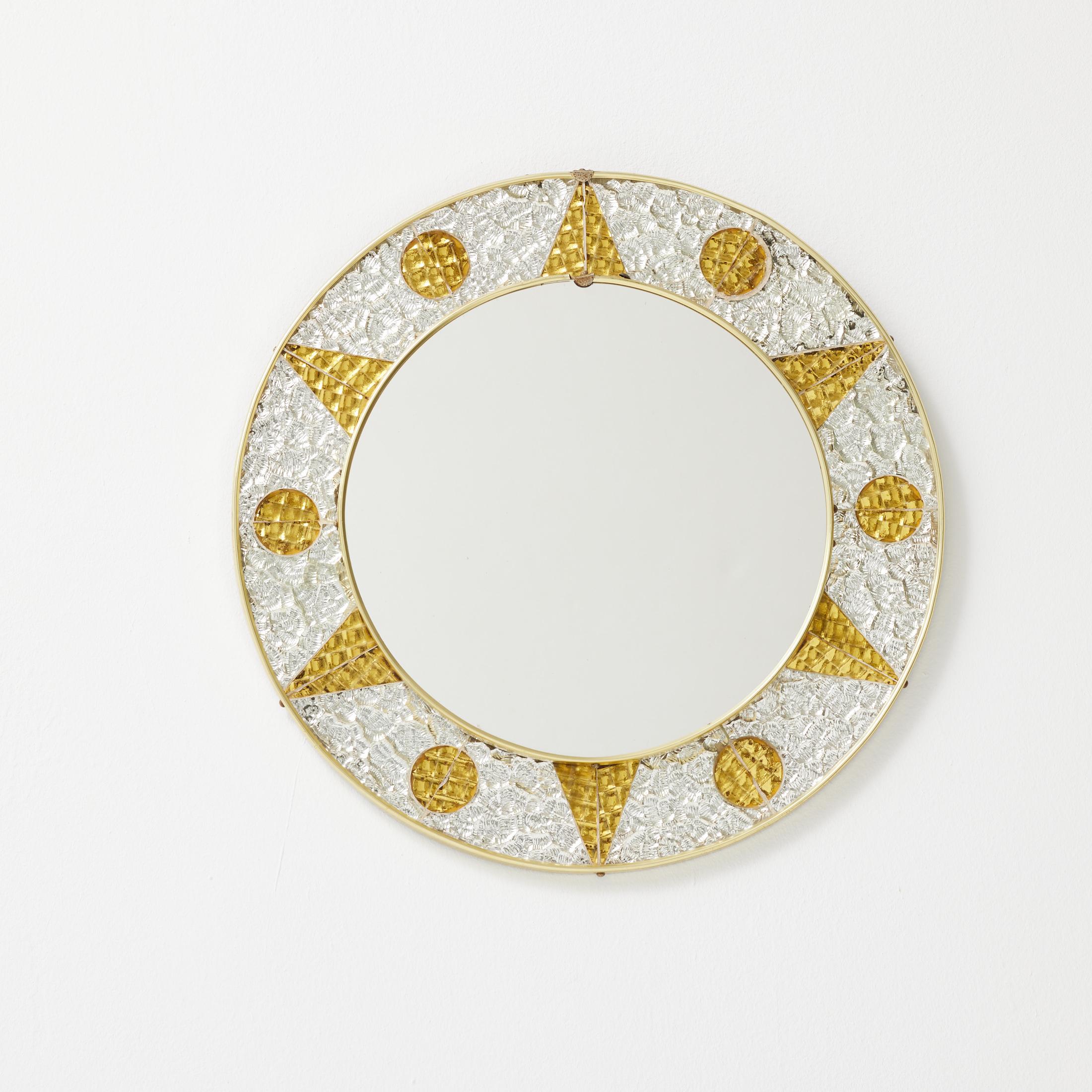 A rare and visually captivating French round wall mirror from the 1960s, featuring a striking decorative frame composed of textured glass in alternating gold and silver tones. The circular border is segmented into geometric forms—triangles and