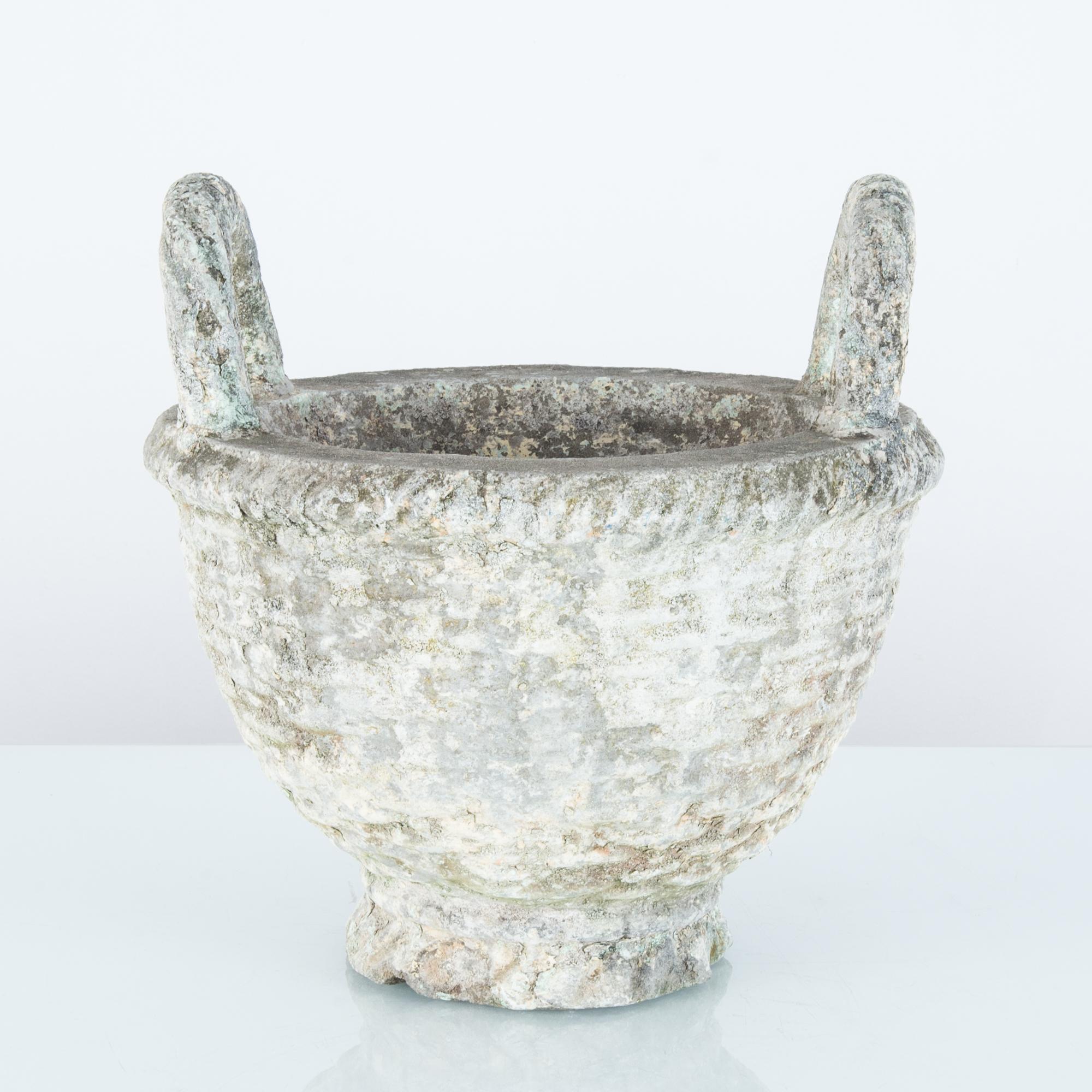 A concrete planter from France, circa 1960. The concrete has been cast into the form of a wicker basket with two upraised handles. Originally painted a creamy white, the surface has weathered into a variegated patina, with accents of lichen yellow