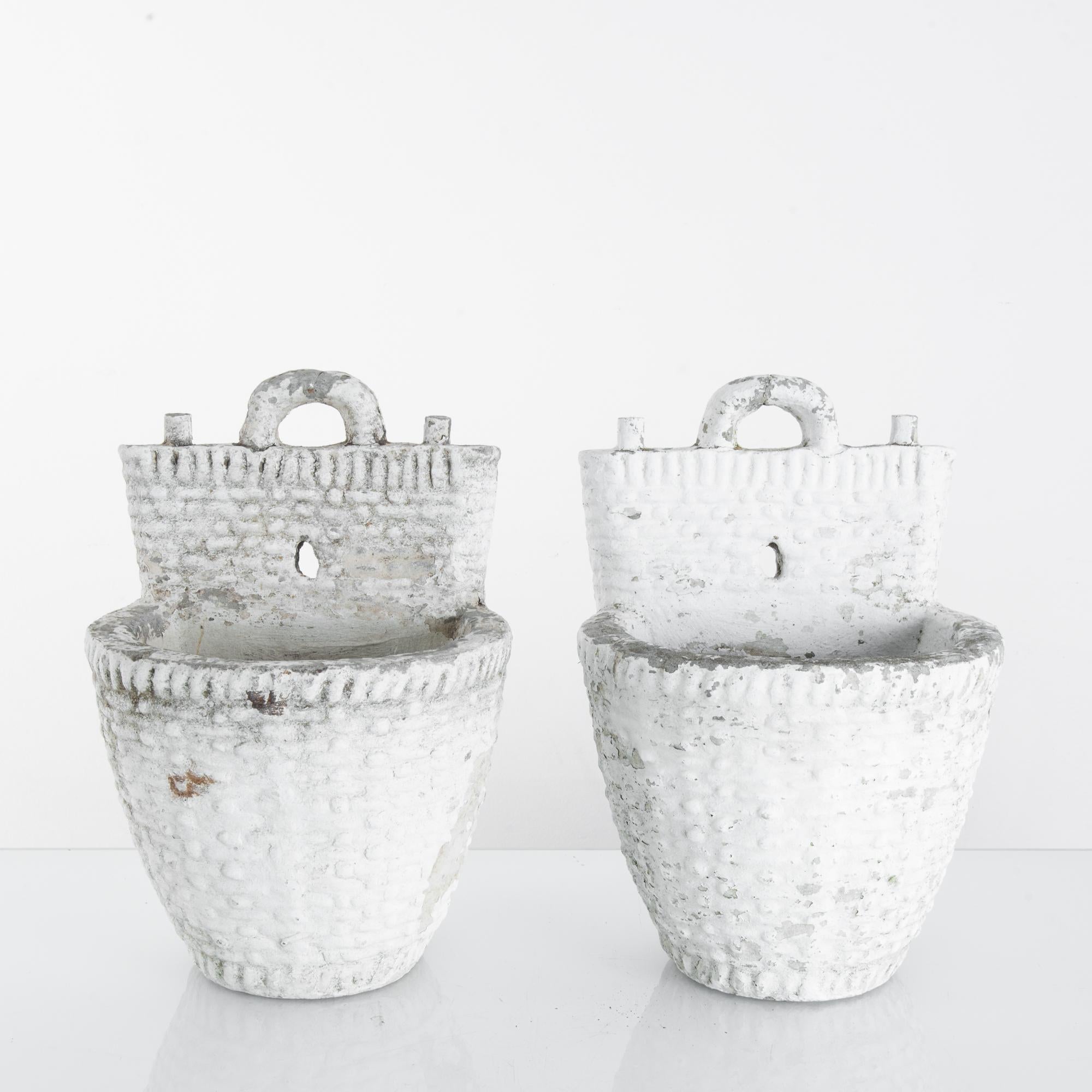 This pair of concrete planters was made in France, circa 1960. Featuring a flat back and a handle on top, the planters can be hung on the wall or simply placed on the ground. With their timeworn patina and moldings of weaving to appear like baskets,