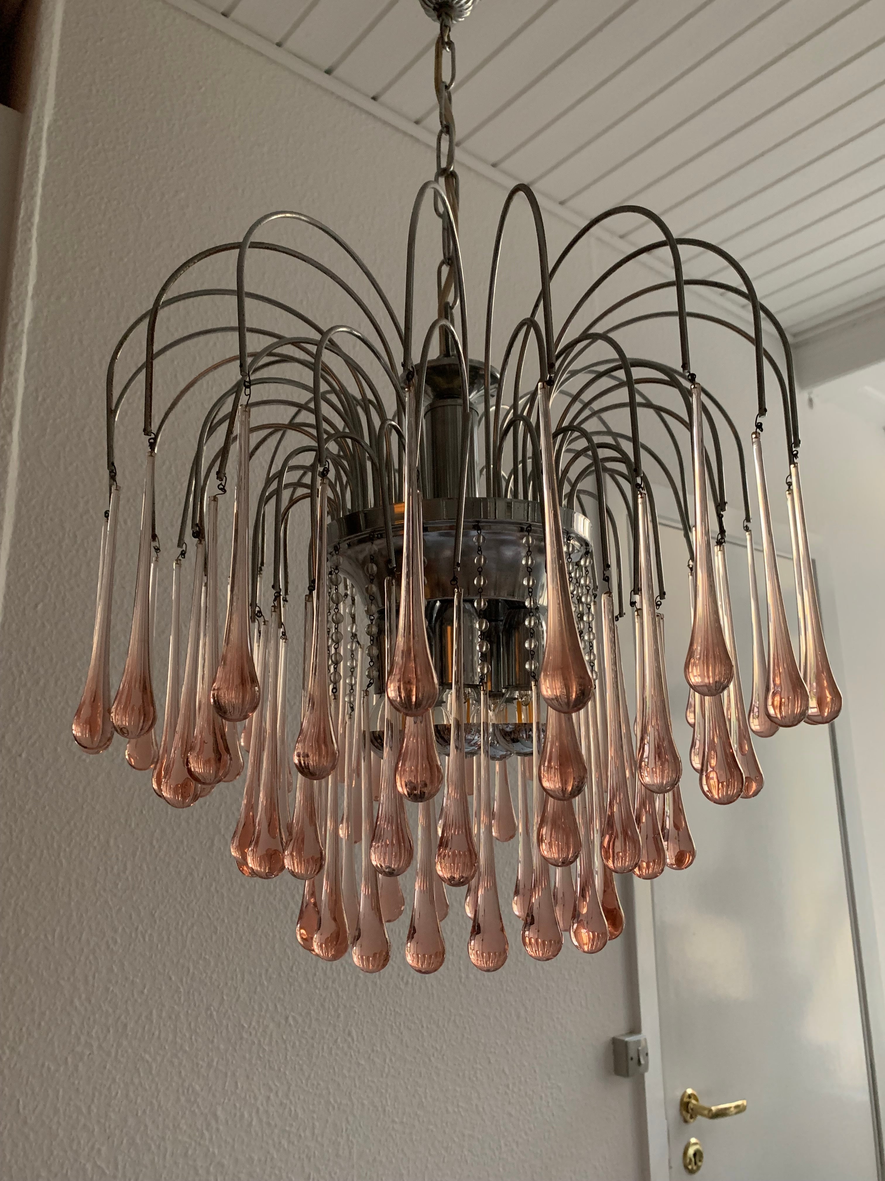 Lampadario francese chic degli anni '60 in cromo con prismi di vetro a forma di goccia rosa e 5 prese elettriche. Il lampadario ha un aspetto leggero, ma emette una buona luce che si riflette magnificamente nei numerosi prismi. Presenta una patina