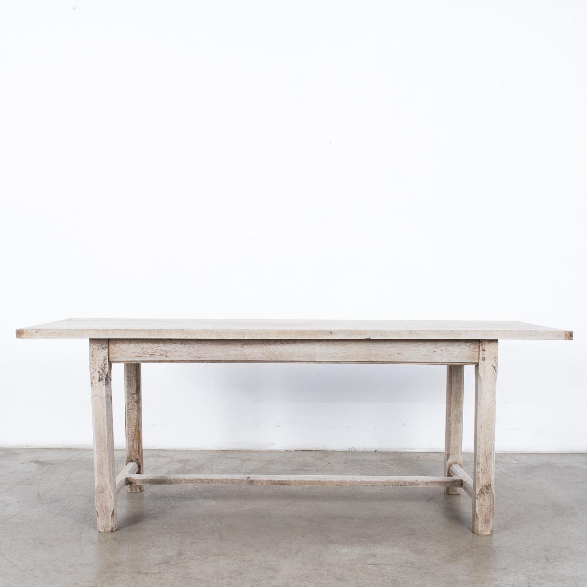 A bleached oak dining table from France, circa 1960. A rectangular tabletop sits atop four legs, joined with a slender strut. The chamfered table legs lend a lithe, decorative touch. The bleached finish of the restored wood emphasizes the lightness