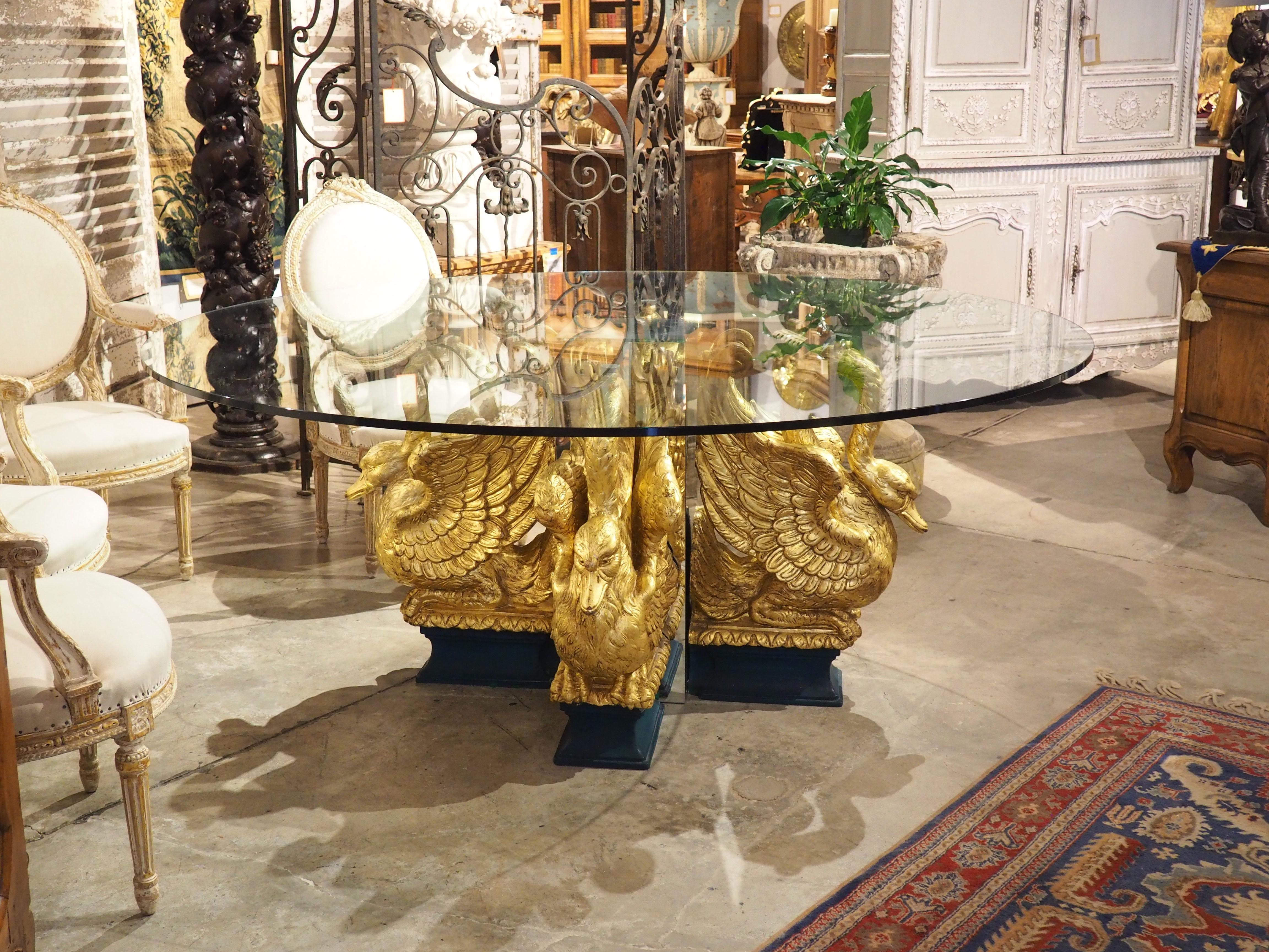 Originario degli anni '60, questo magnifico tavolo da centro o da pranzo francese faceva parte della collezione Claude Montana. Il tavolo ha un piano circolare in vetro spesso mezzo pollice sostenuto da quattro cigni dorati su zoccoli verde foresta