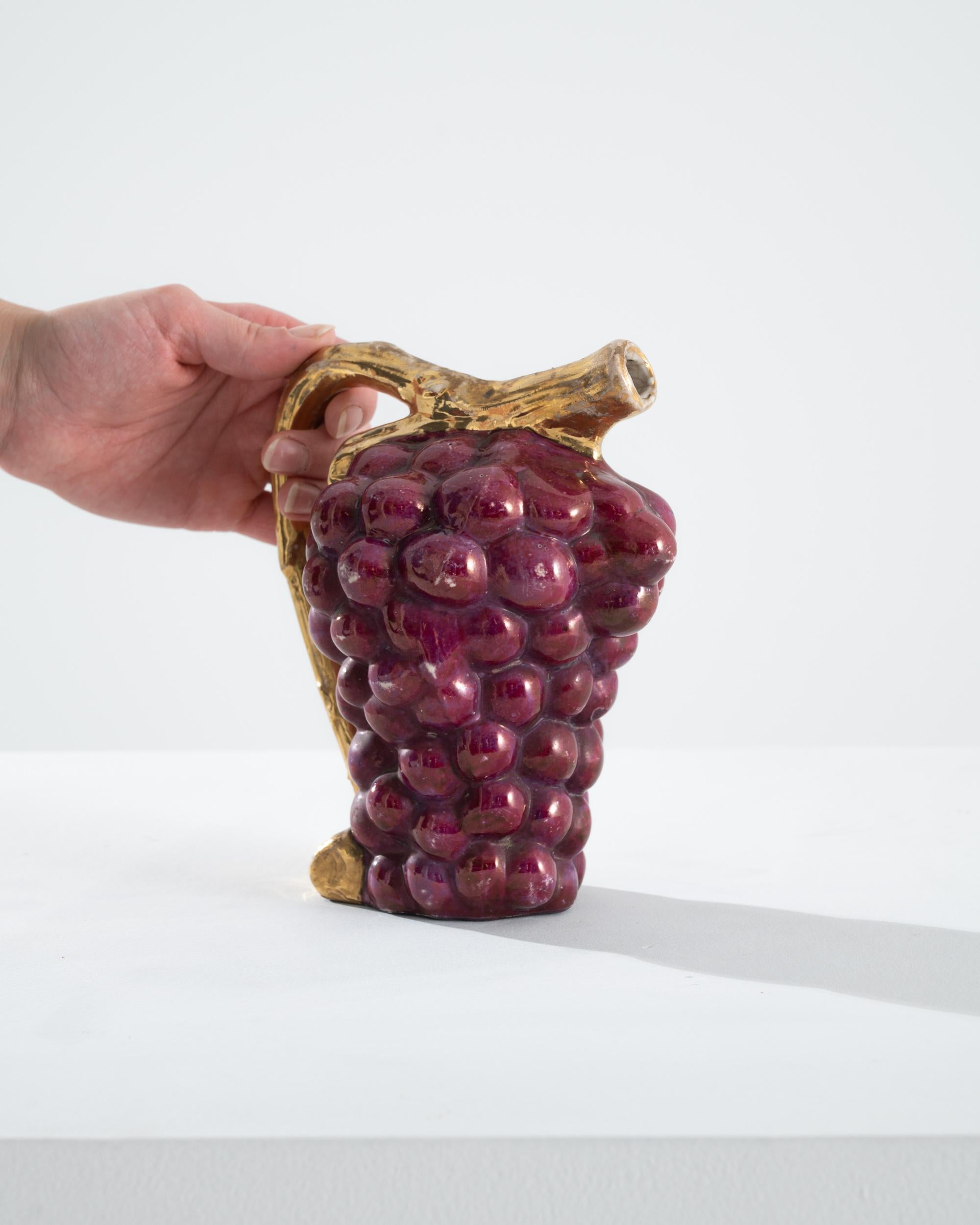 A ceramic pitcher from France, produced circa 1960. This sculpted pitcher is modeled into the distinctive shape of a grape canopy, suggesting the vessel's continents. Appearing with a domestic nostalgia, the playful shape is adorned with a gilded