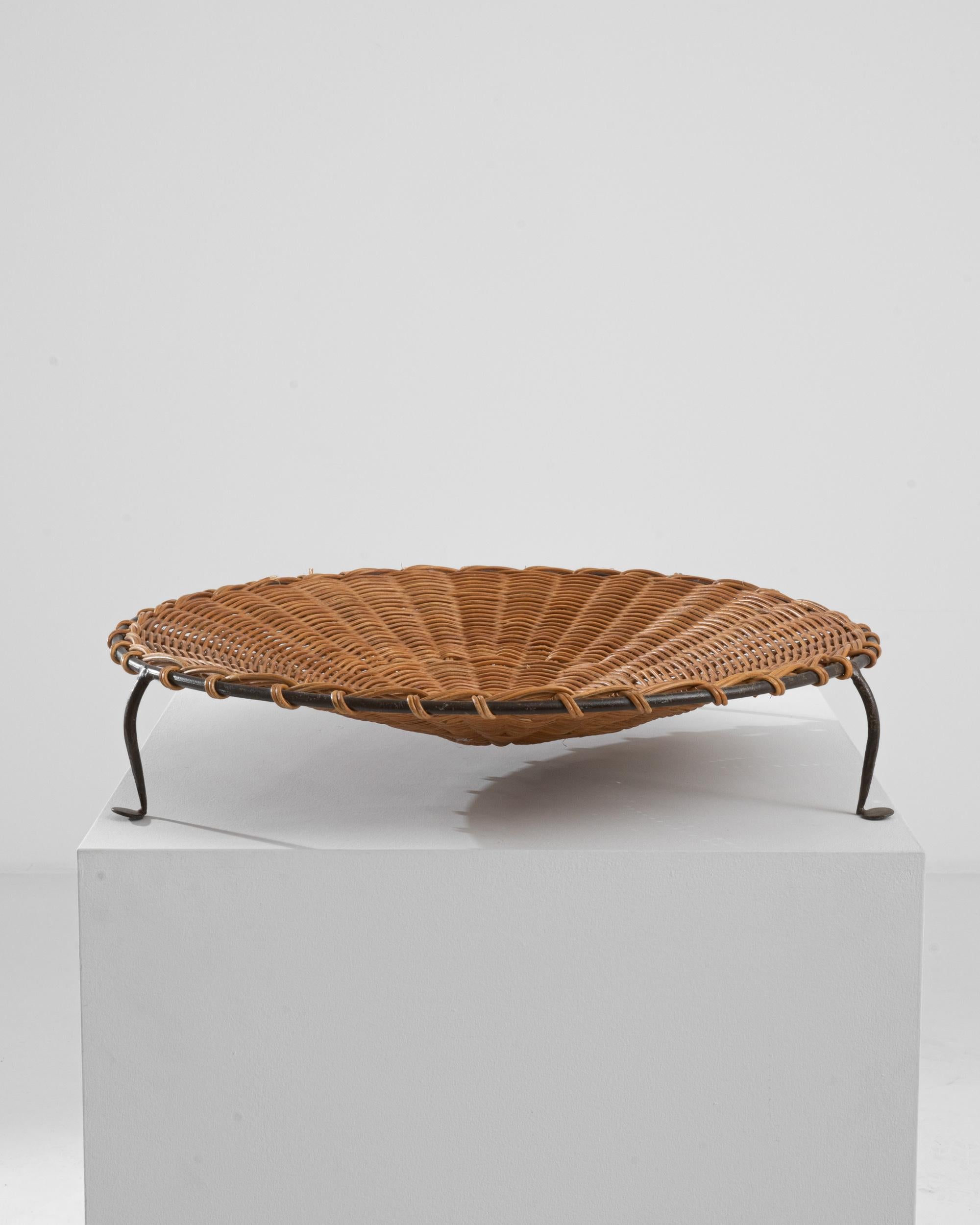 This vintage platter was made in France, circa 1960. A low bowl with an elevated base, the woven Material finds its unlikely mate in the metal structure. Radiating 60s charm, the metal feet give an anamorphic quality. Cane is woven into a concentric