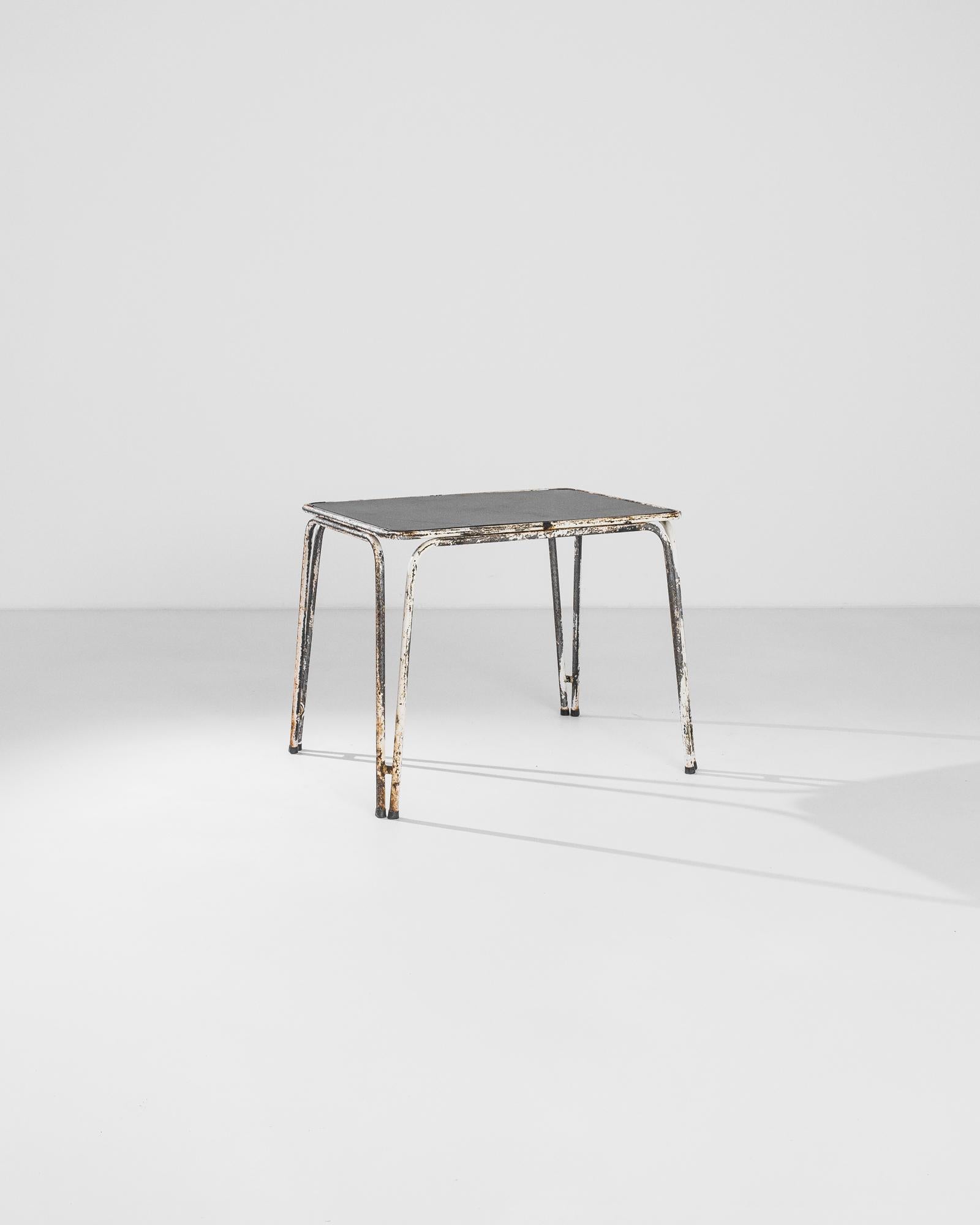 A metal garden table from France, produced circa 1960. White patinated bent metal legs support a black tabletop in this table built for relaxation. Imagine: lounging under the sun in tennis whites, not a court in sight, as condensation from an