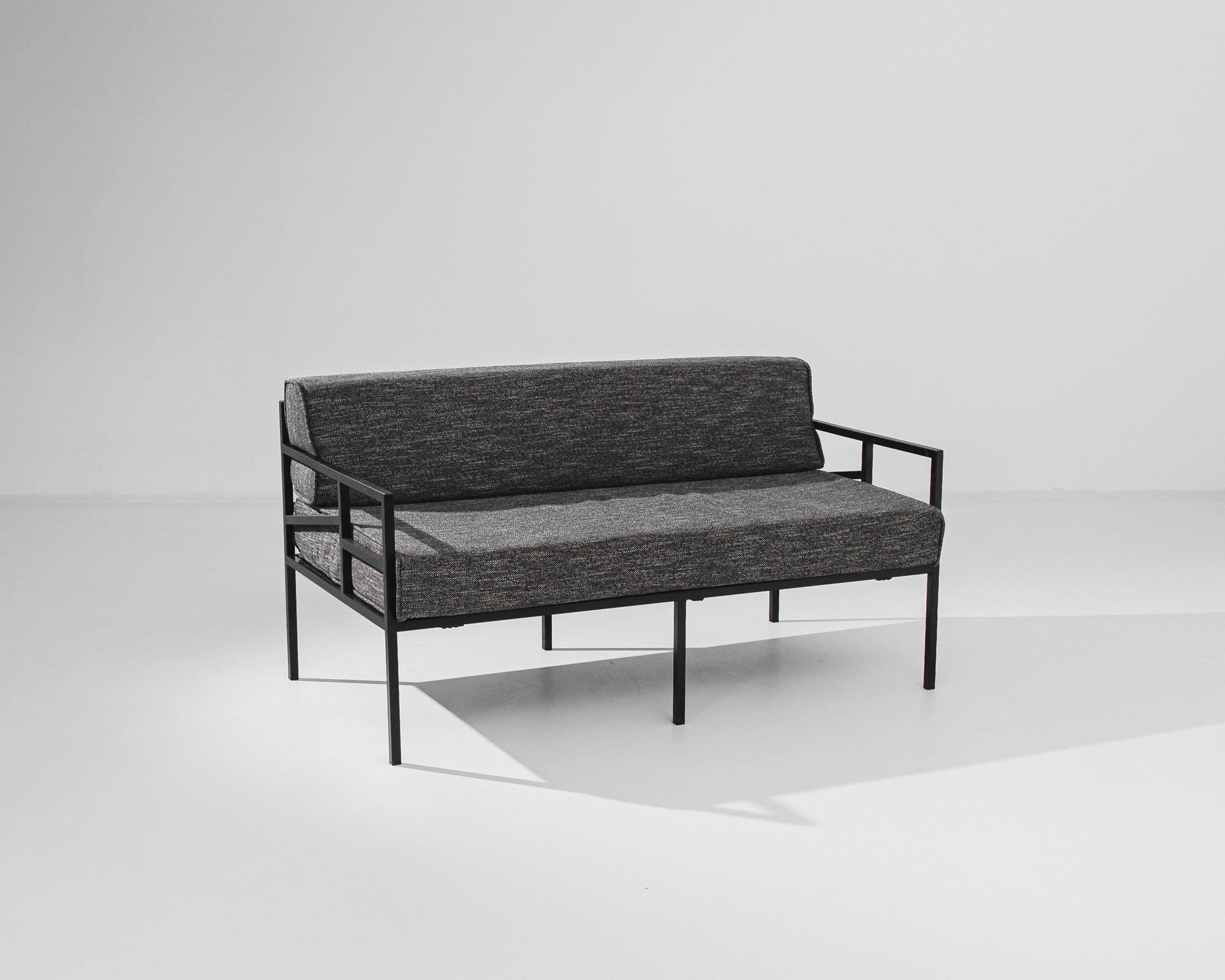 A metal sofa with upholstered seat and back produced in France circa 1960. A vintage sofa of thick, heather grey cushions set upon a deep, black metal frame with six, thin legs. The bold profile of the cushions grounds the otherwise light and airy