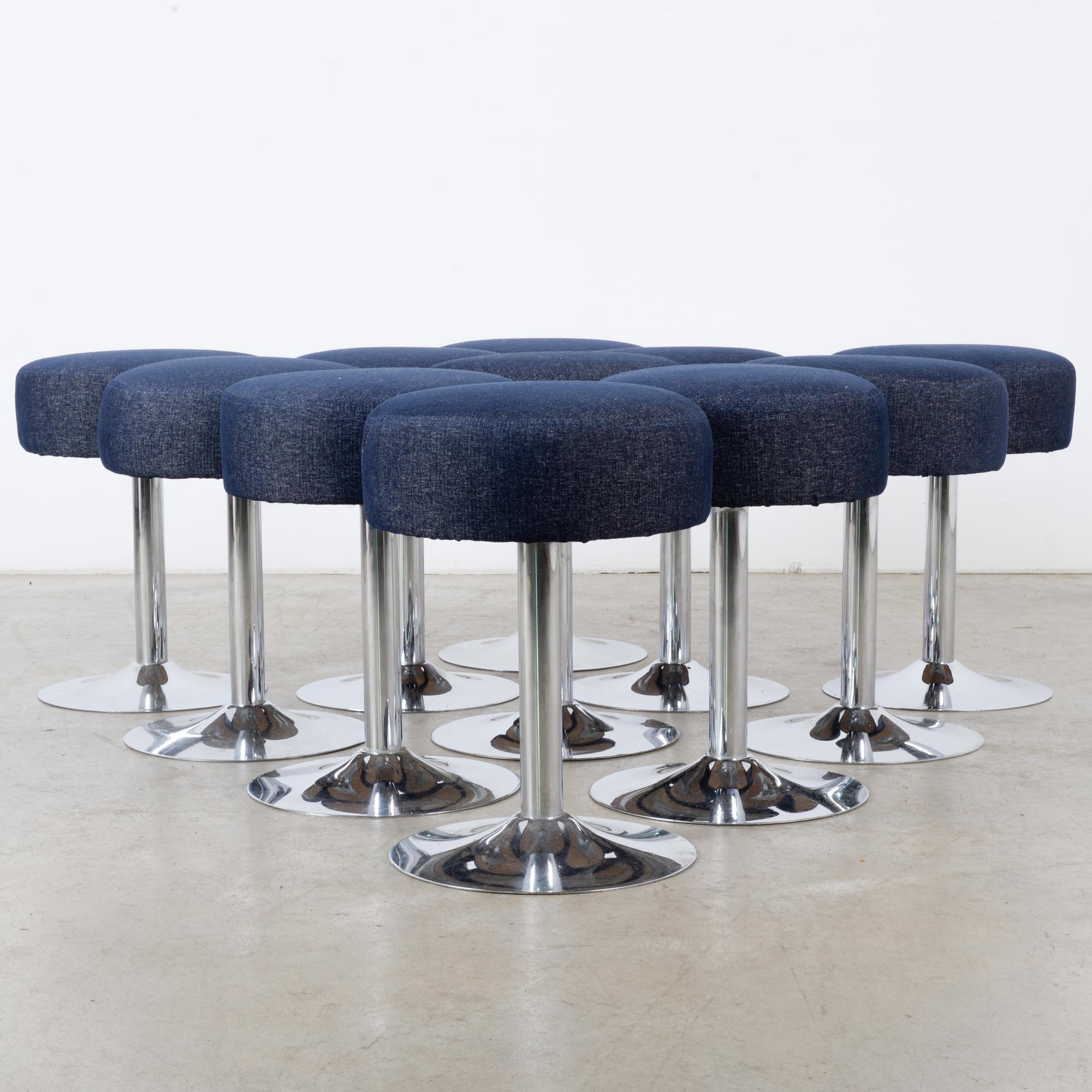 A set of eleven metal stools with upholstered seats from France, circa 1960. Pedestals of bright reflective metal support circular seats, upholstered in an indigo blue. The clean lines are suggestive of Space Age design. The deep color creates an