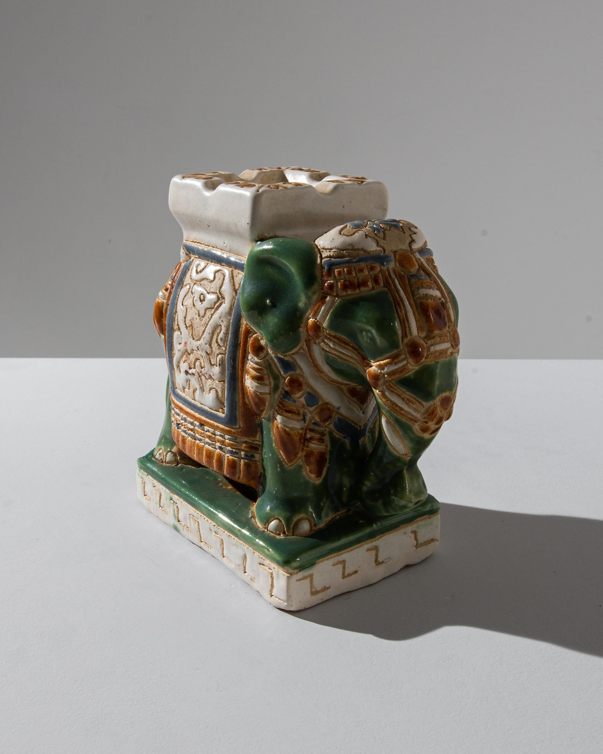 A ceramic decoration from 1960s France in the shape of an elephant. A saddle seat and blanket are glazed with celadon hues, laced with powder blue and a wash of yellow ochre; the assortment of delicate patterns — reflecting Chinese and Arabic