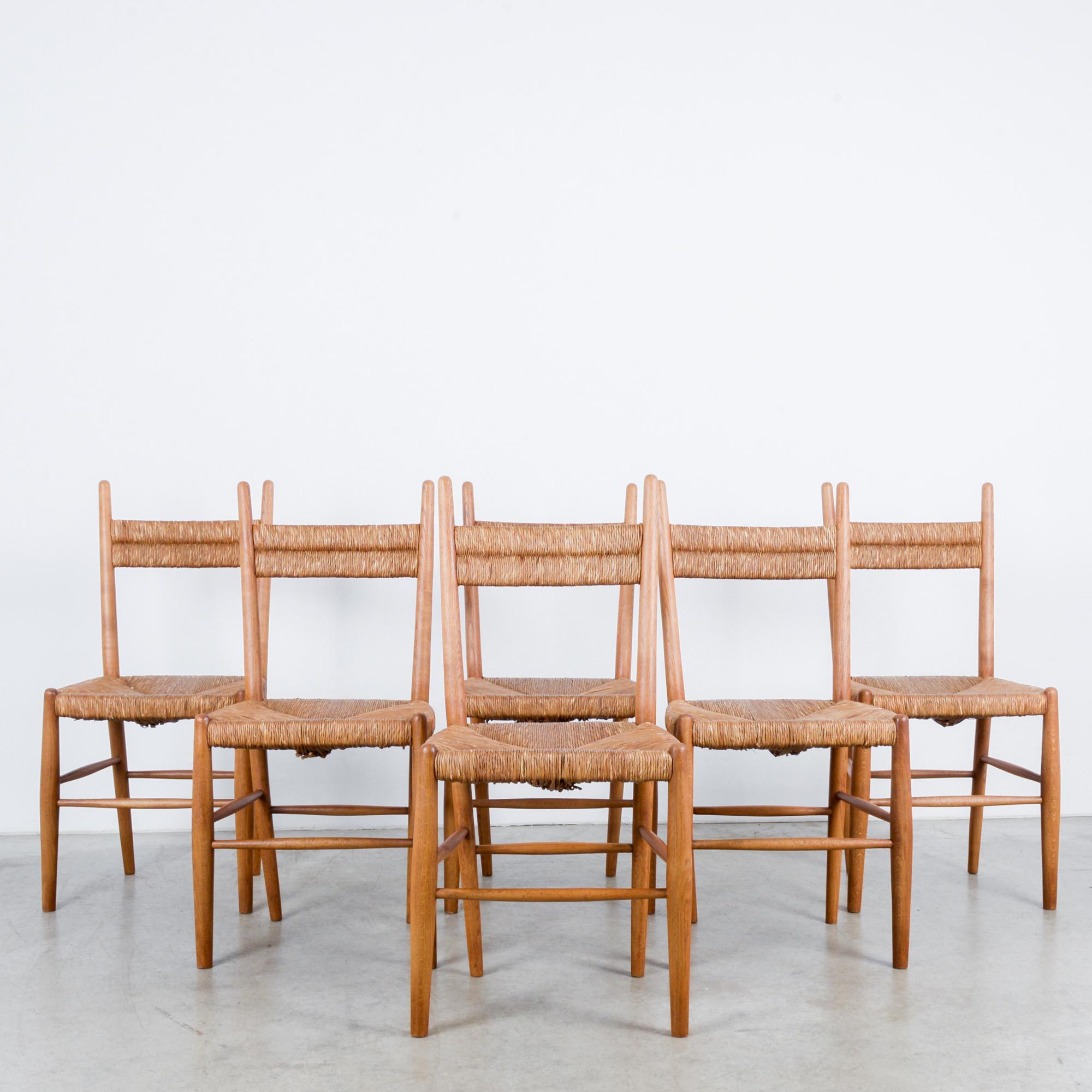 A set of six wooden chairs with woven rush seats and backs from France, circa 1960. Softly rounded barrel legs connected by simple offset stretchers form smooth, clean lines designed to support the body naturally. Combination of natural fiber and