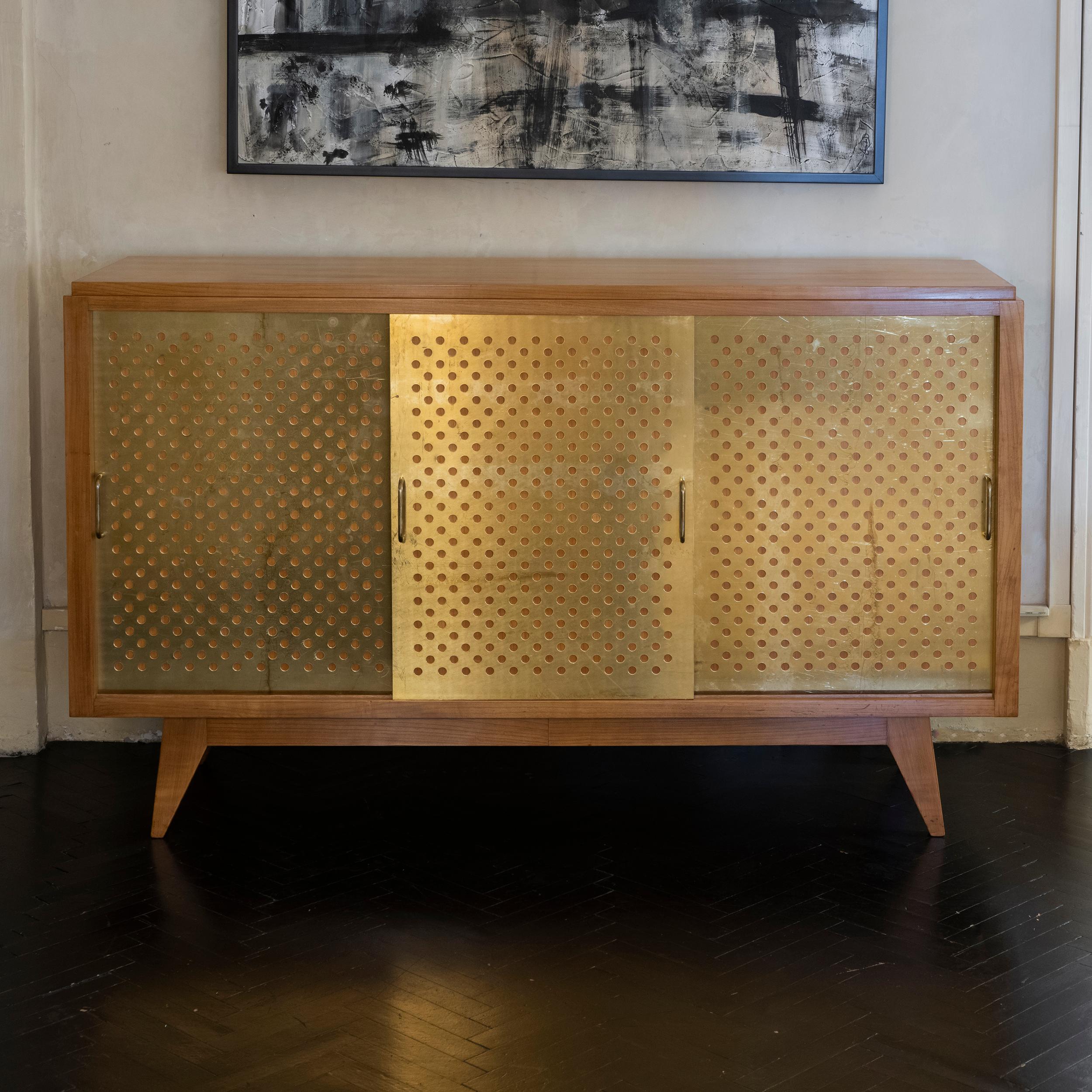 1960's French Oak sideboard, in perfect condition and vintage patina, three sliding doors with decorative panels in perforated brass inspired by the work of Jean Prouvé, two adjustable shelves inside.