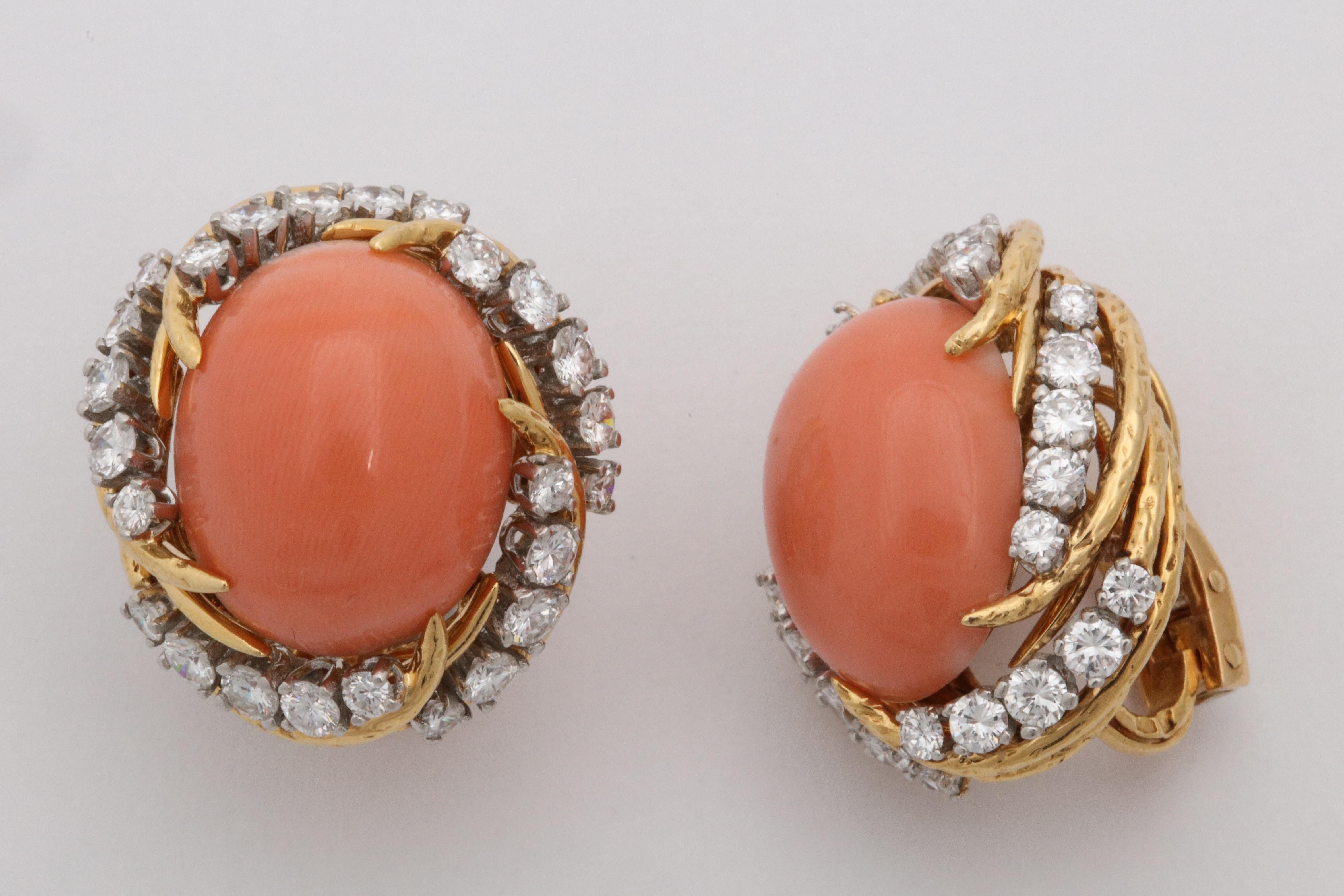 One Pair Of Ladies Elegant Swirl Design Earclips Created In 18kt Textured Gold Setting. Earrings Are Further Designed With Two Large Oval Cut 17MM Cabochon Coral Stones. Corals Are Surrounded By Numerous High Quality Full Cut Diamonds Weighing