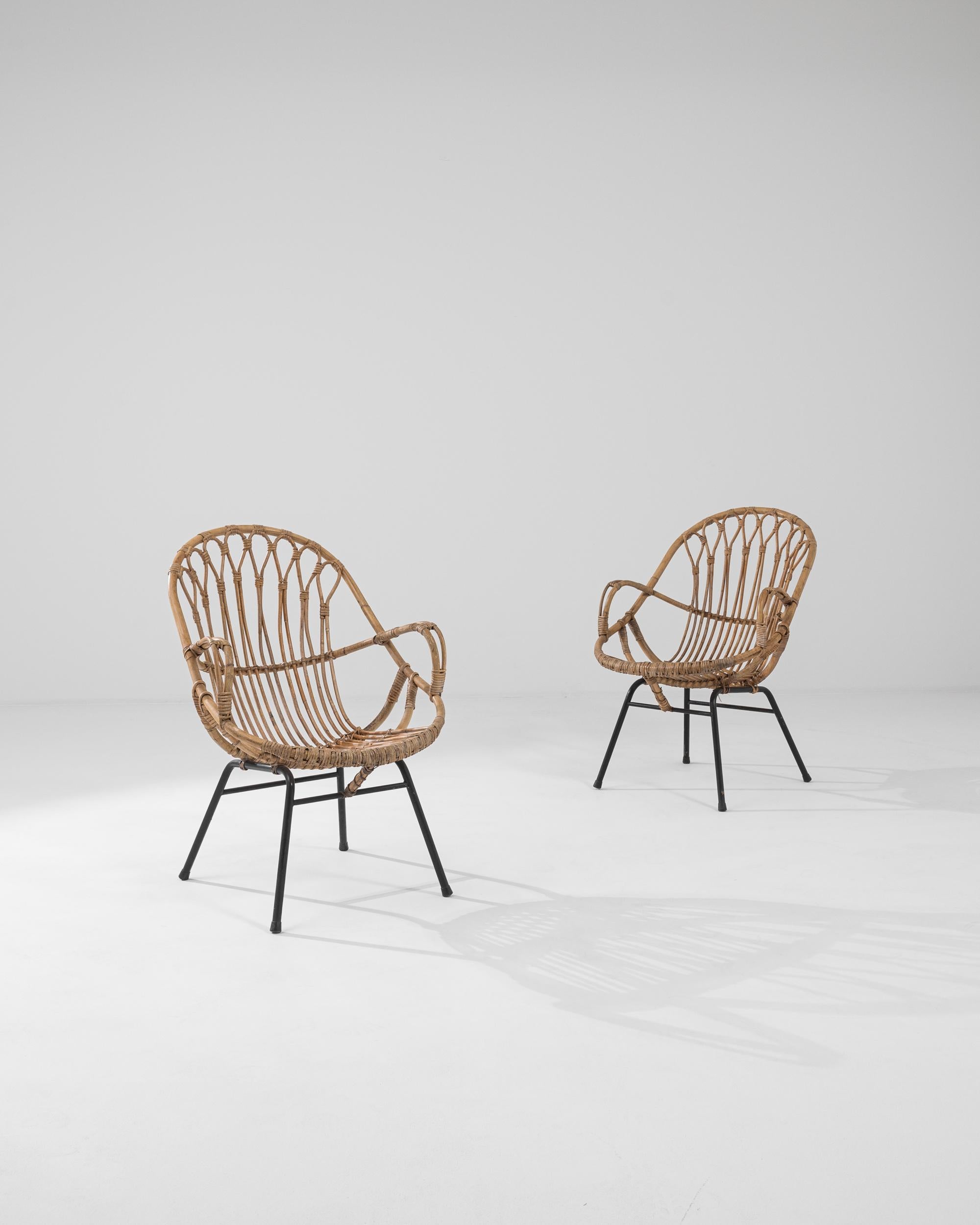 A pair of armchairs from France, circa 1960. These french-made armchairs are a playful twist on a midcentury classic. Using lashed together rattan, artisans have crafted a chair both geometrically pleasing and surprisingly comfortable. Created by