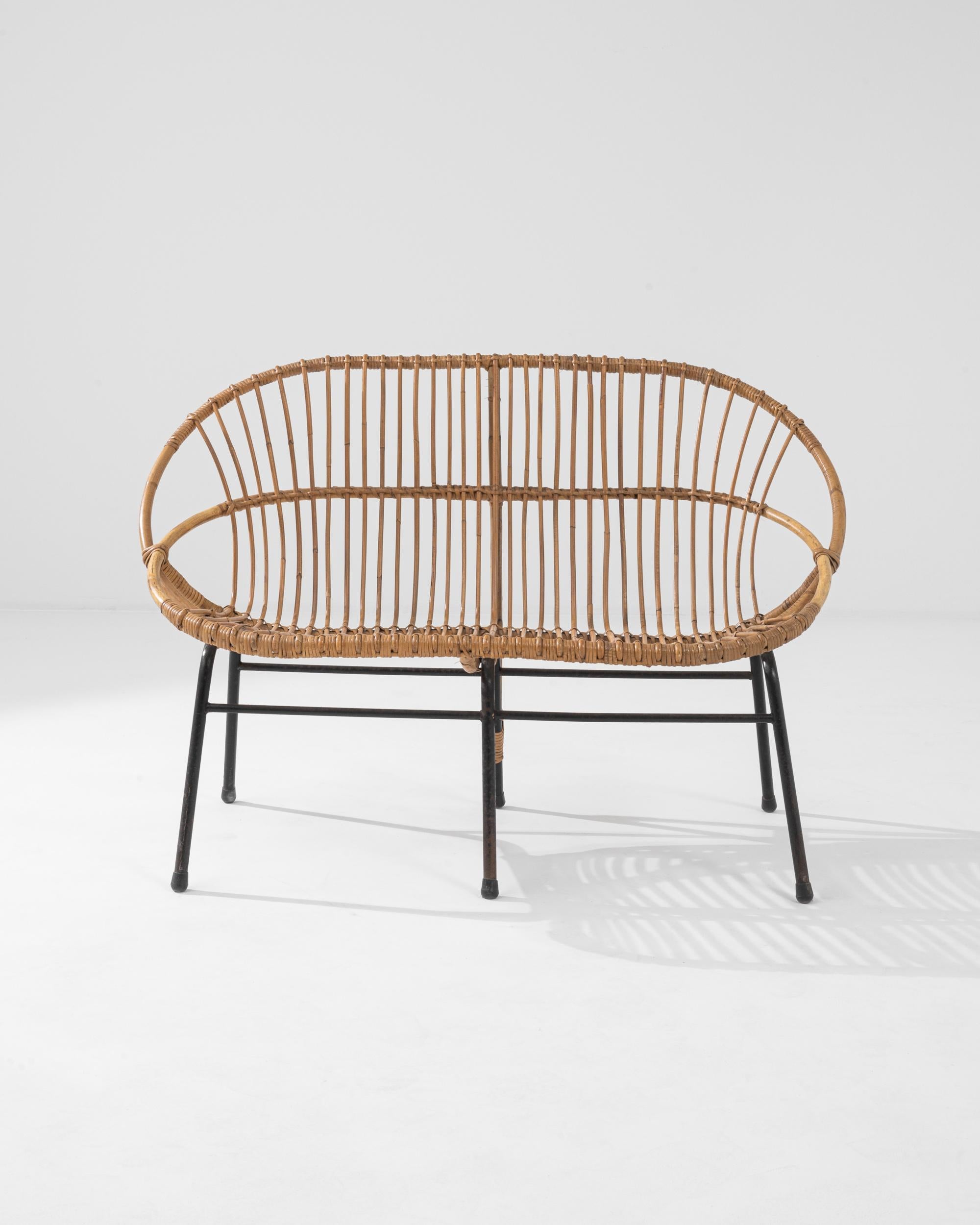 A wicker settee from France, circa 1960. This French-made bench is a playful twist on a mid-century classic. Using lashed together rattan, artisans have crafted a chair both geometrically pleasing and surprisingly comfortable. Created by bending